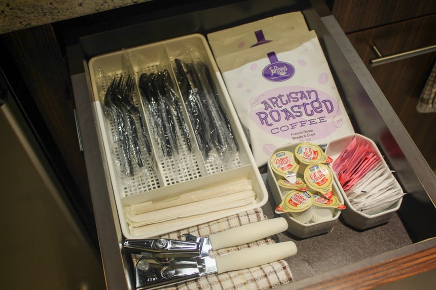 a drawer with in room amenities like coffee, creamer, plastic ware, and more