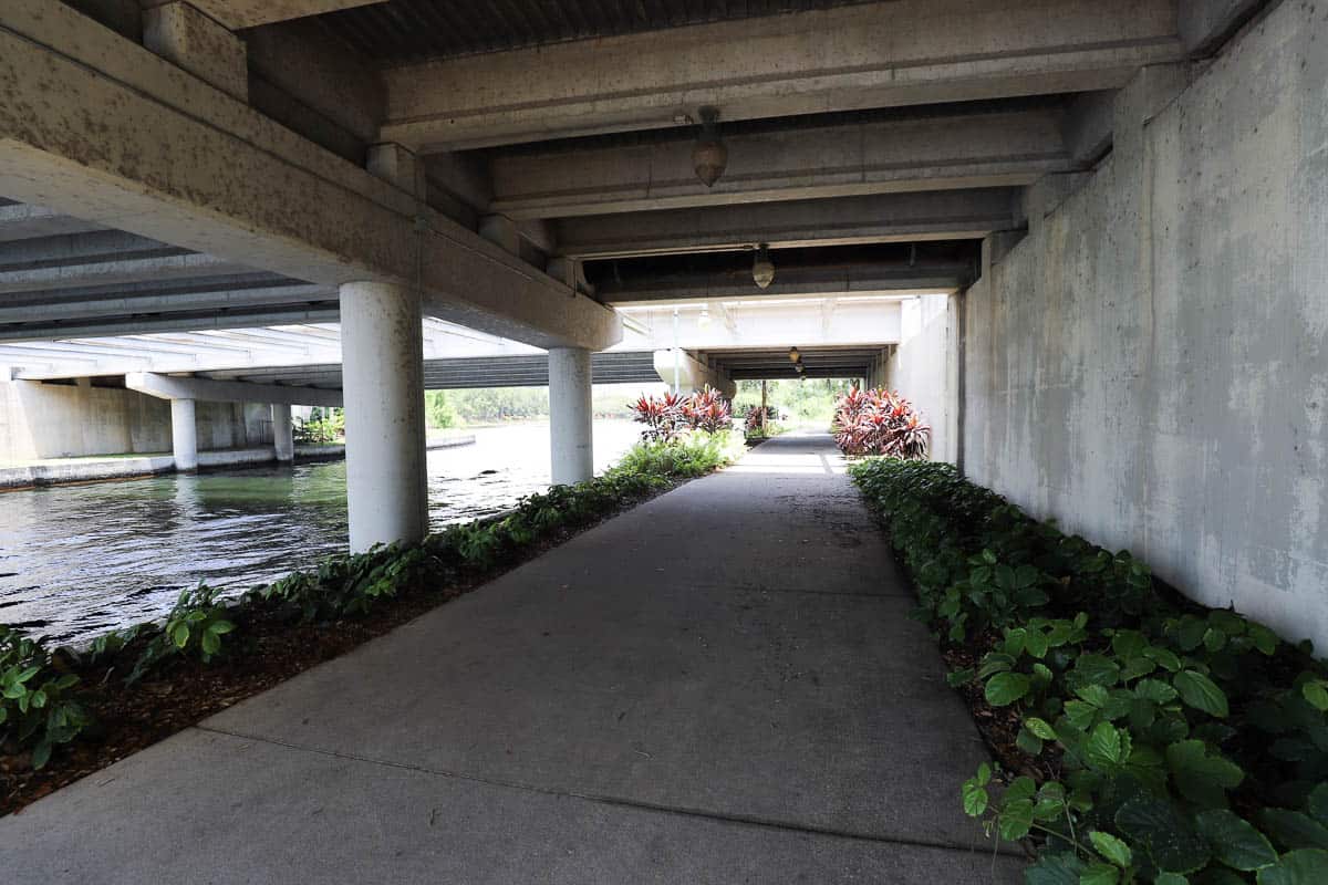 The sidewalk continues under the overpass or bridge above. 