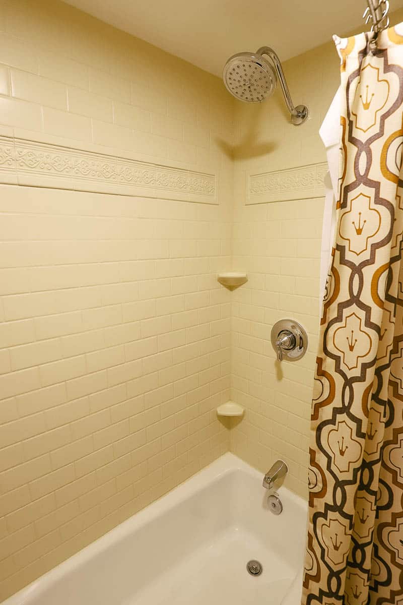 a shower head with a few places to store items in the shower and a shower curtain with tiny frog crowns 