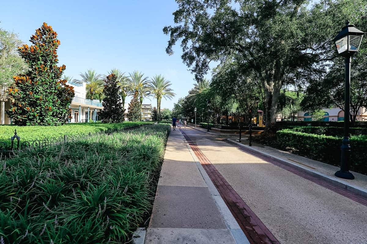 a walkway that leads through the French Quarter at Disney World with green grass and sidewalks 