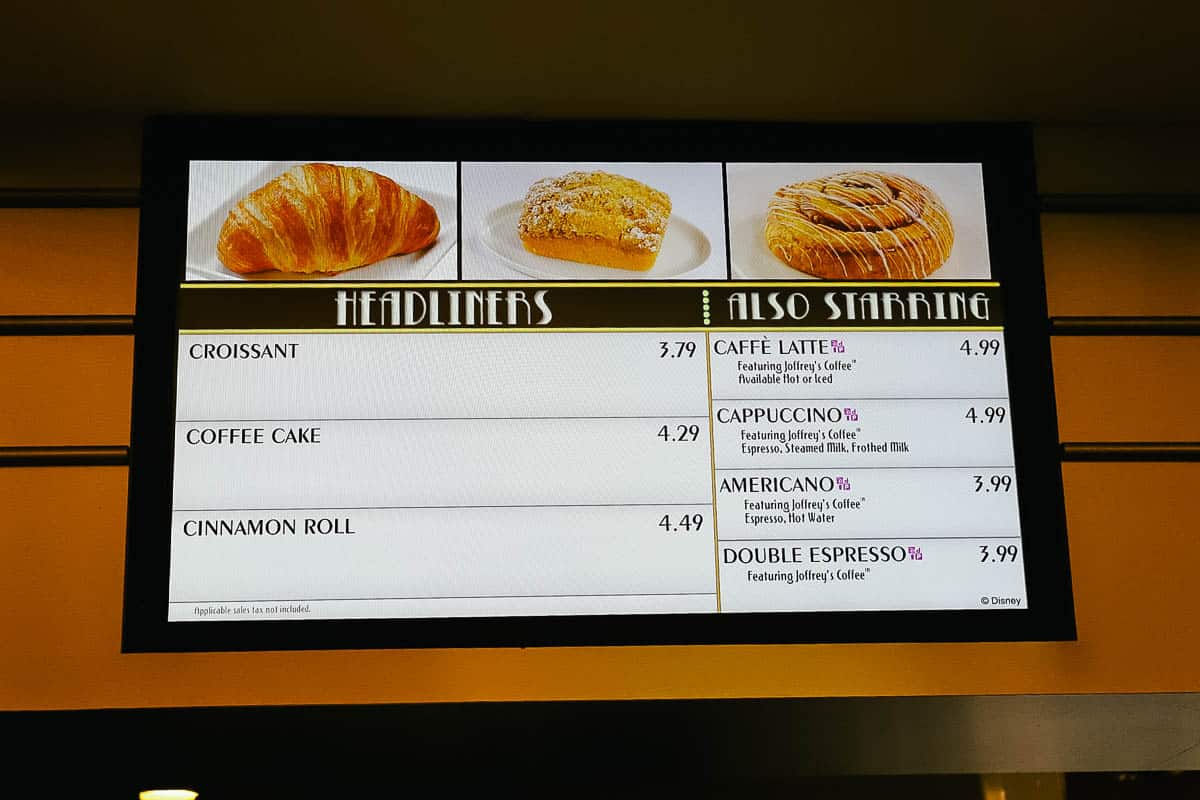a menu board with croissants, coffee cake, cinnamon rolls, and coffee including specialty coffee at All-Star Movies Food Court 