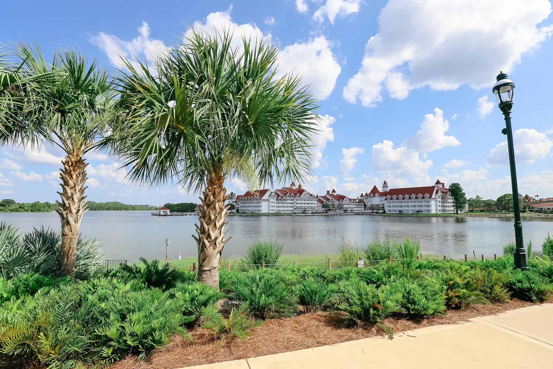 A view of two palm trees on the walkway with the Seven Seas Lagoon and Grand Floridian in the distance. 