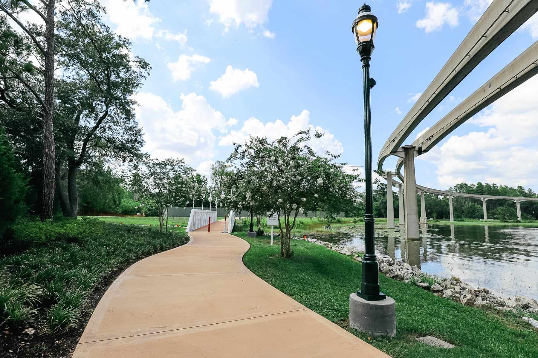 the walking path with a light pole on the right and a white bridge ahead 