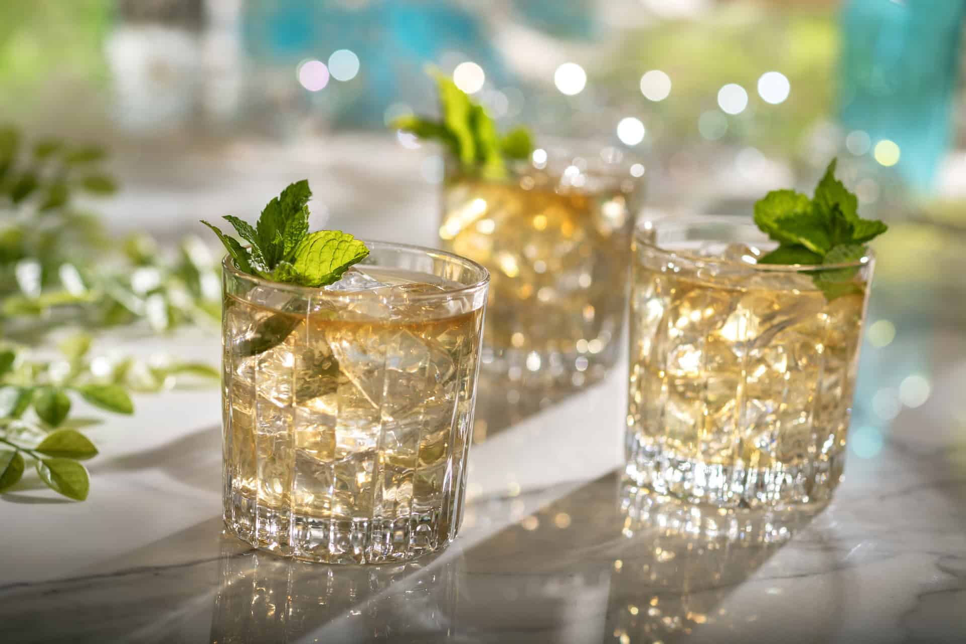 three glasses with gold colored beverages topped with mint
