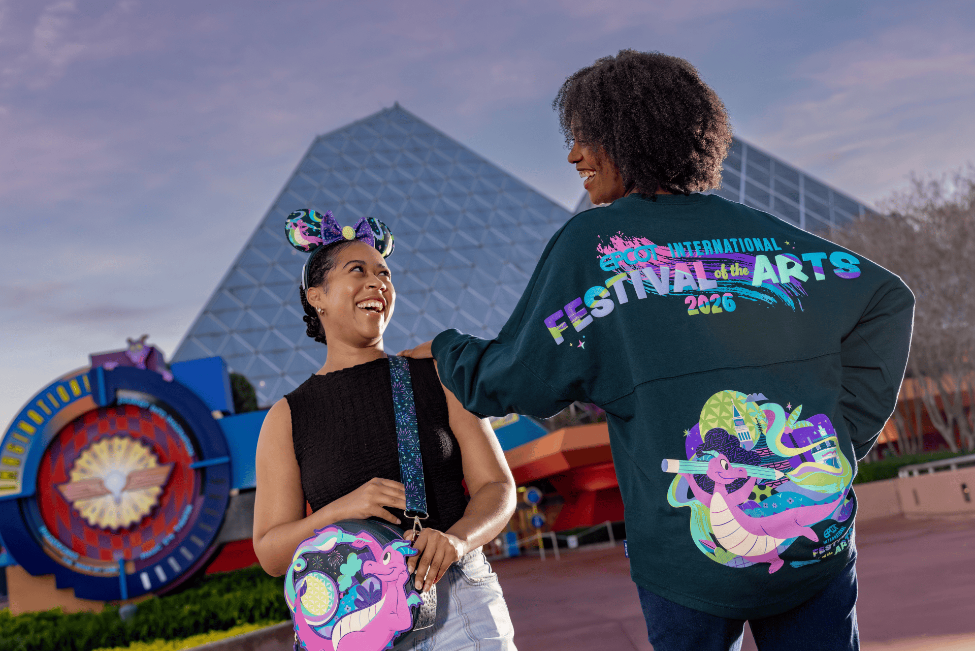a person wearing a Loungefly Figment bag, a Minnie Ear headband standing next to a person modeling the 2026 Festival of the Arts spirit jersey