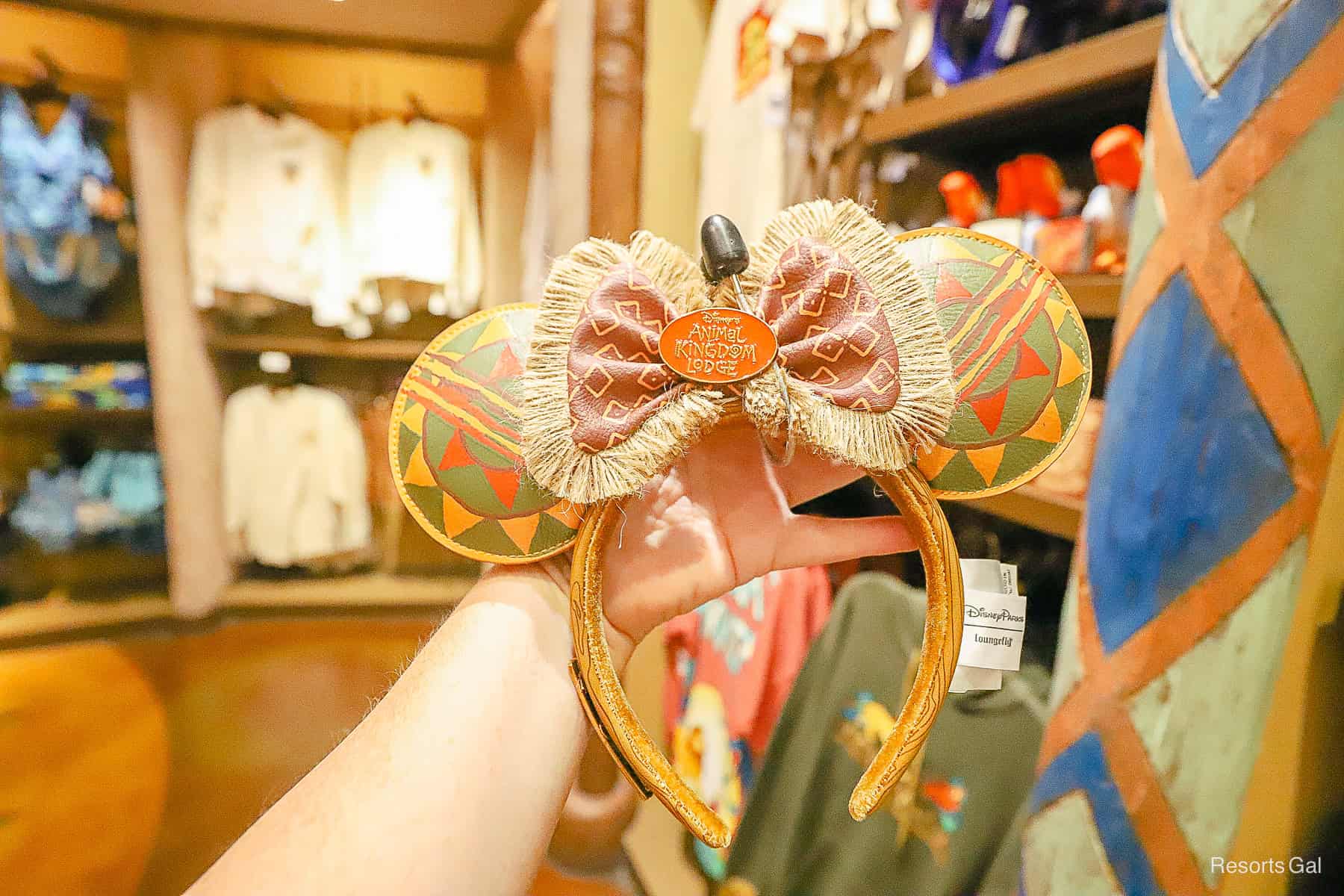 a hand holding a pair of Disney's Animal Kingdom Lodge ears in green, yellow, and orange with a bow 
