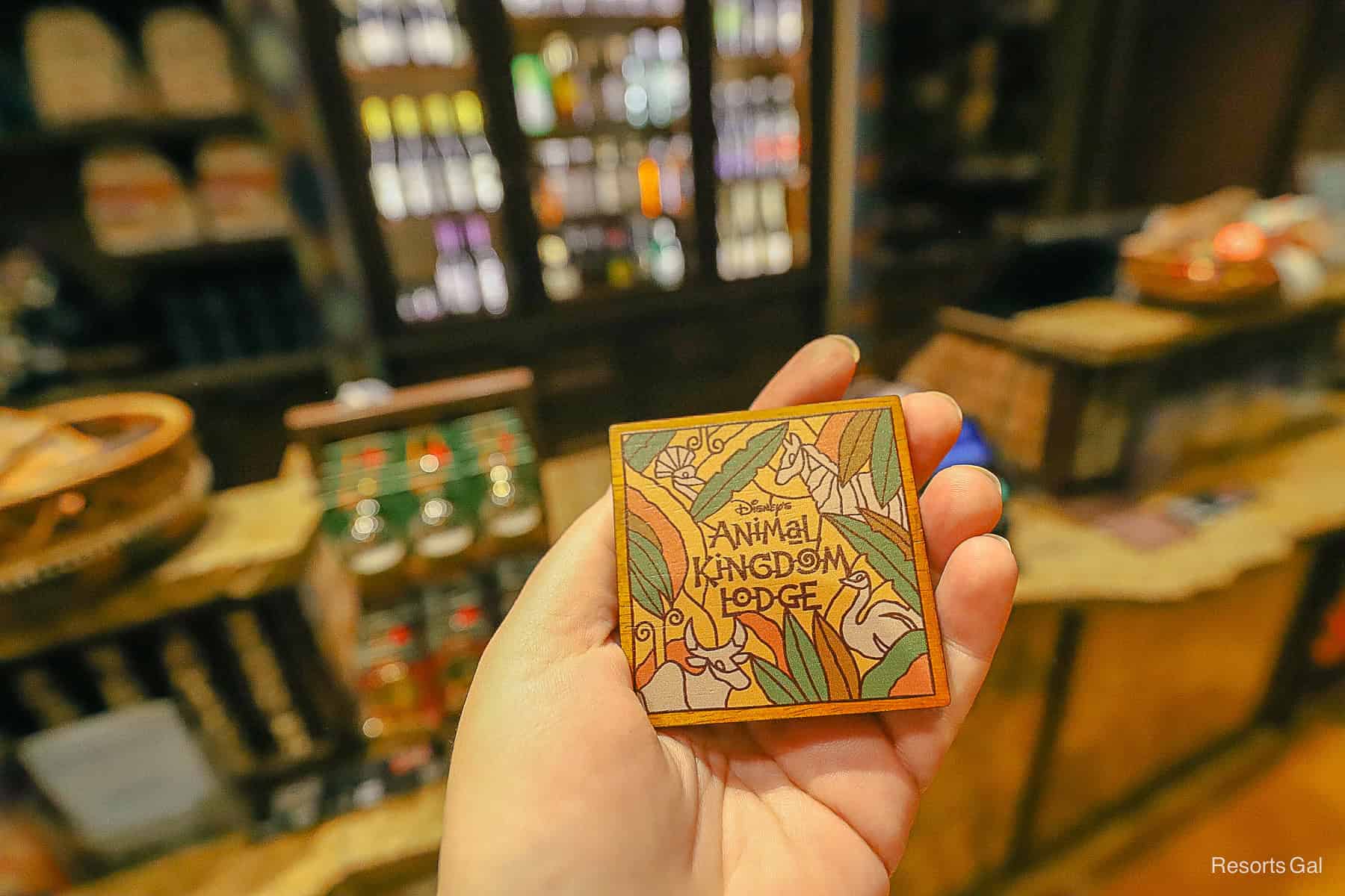 a hand holding a new Disney's Animal Kingdom Lodge magnet that has a wooden look with animal print 
