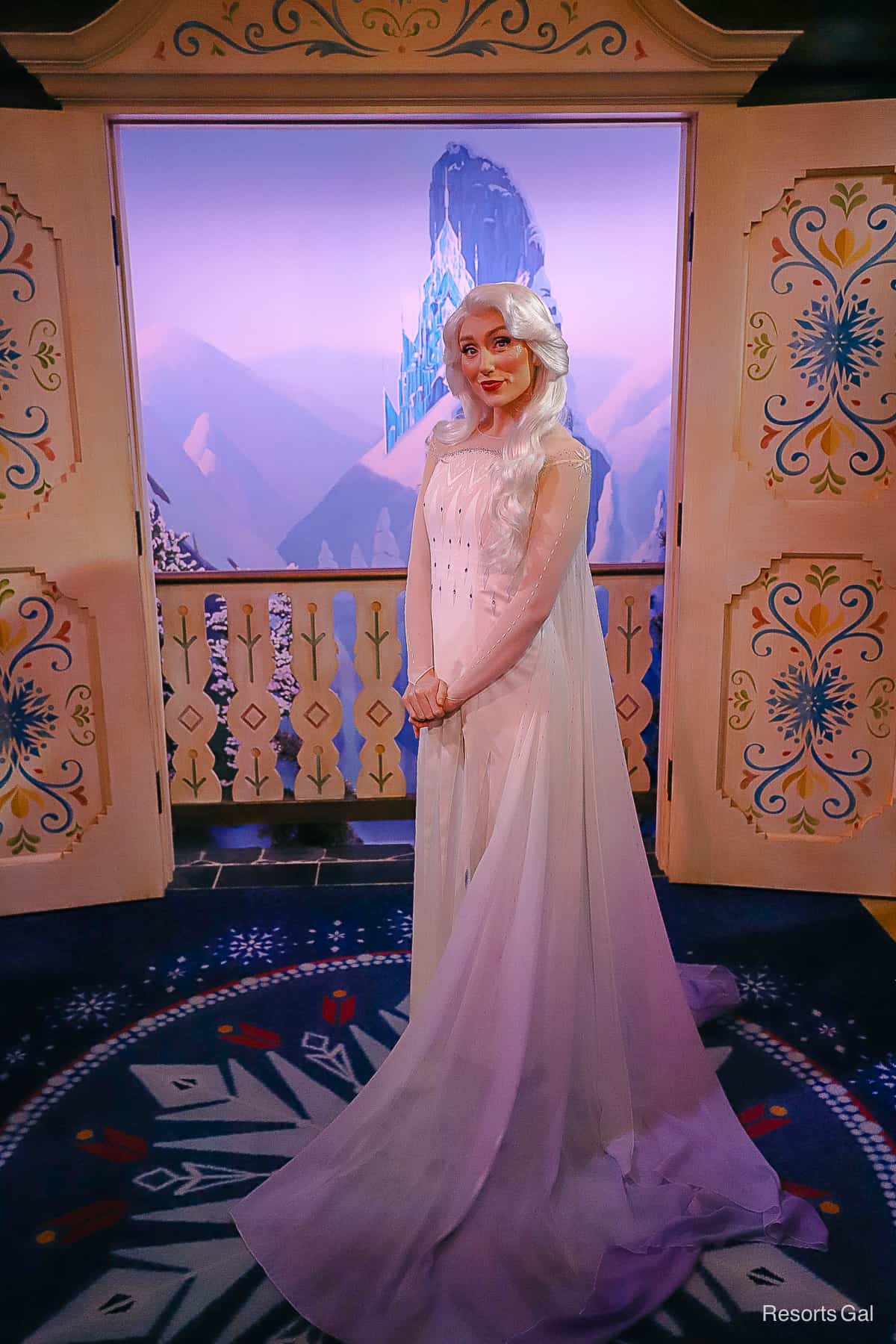 Elsa poses with her hands folded wearing her white gown. 