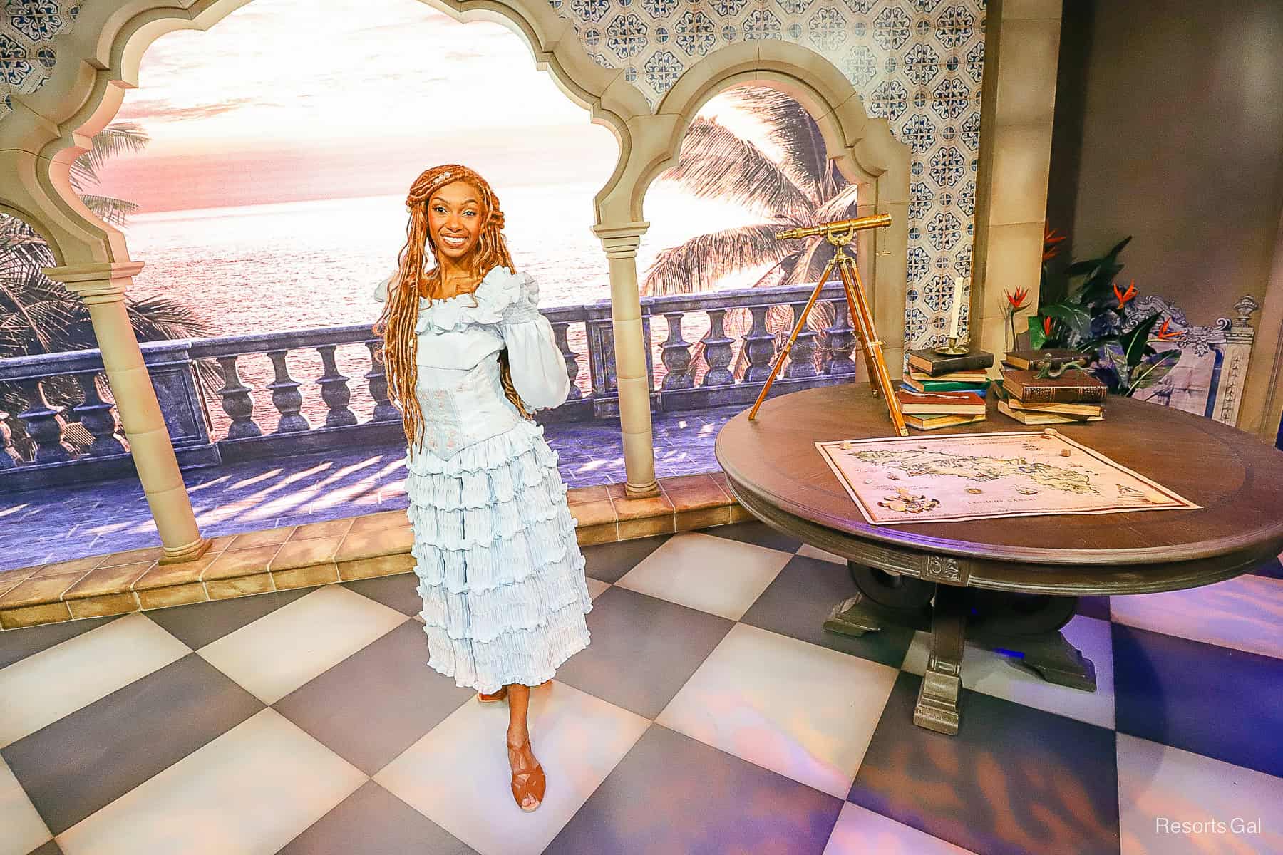 Ariel next to a table with props from Prince Eric's library. 