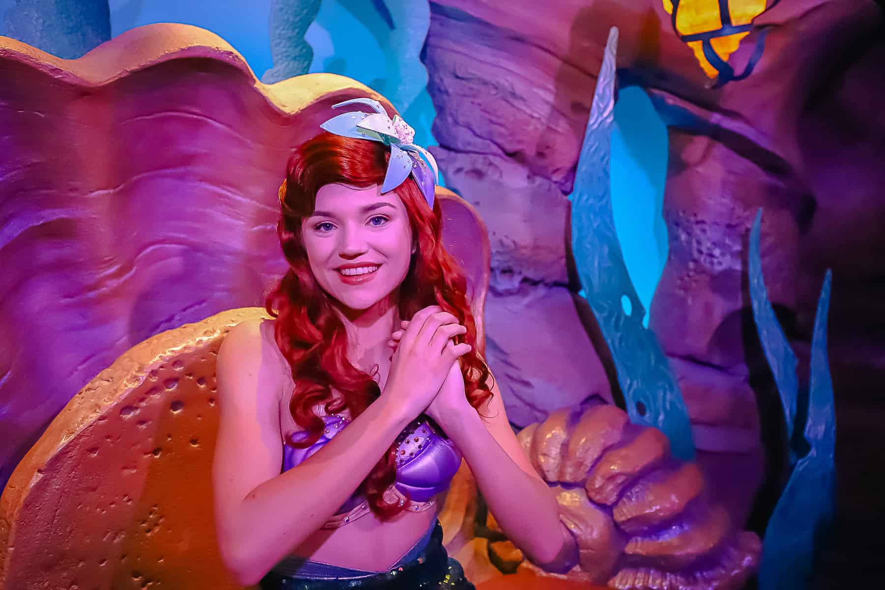 Ariel poses with her hands clasped to the right of her face. 