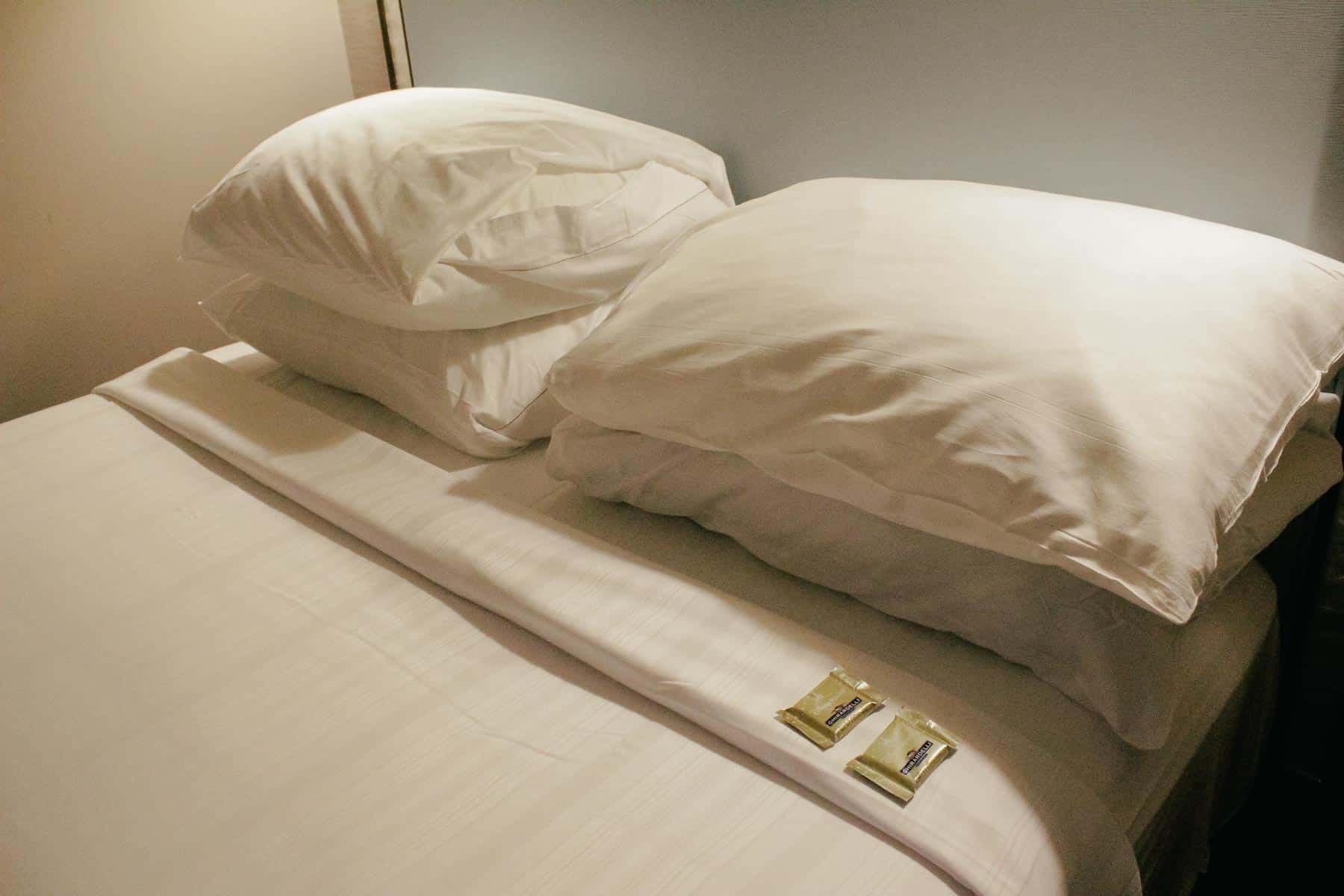 a bed with the covers folded down and chocolates left near the pillows 