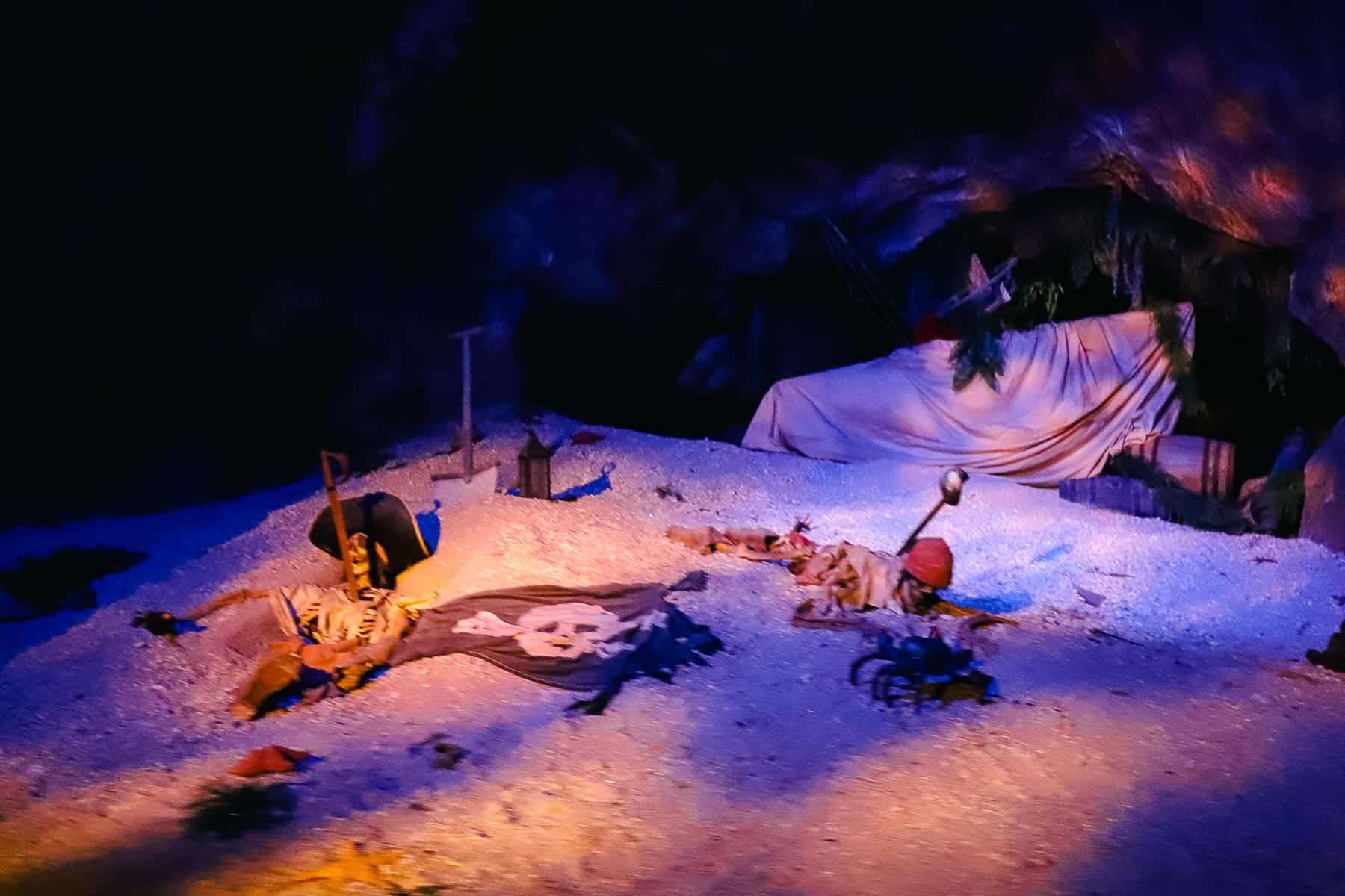 Shows the skeletons of pirates on a beach with pirate flags in the first scene of the ride. 