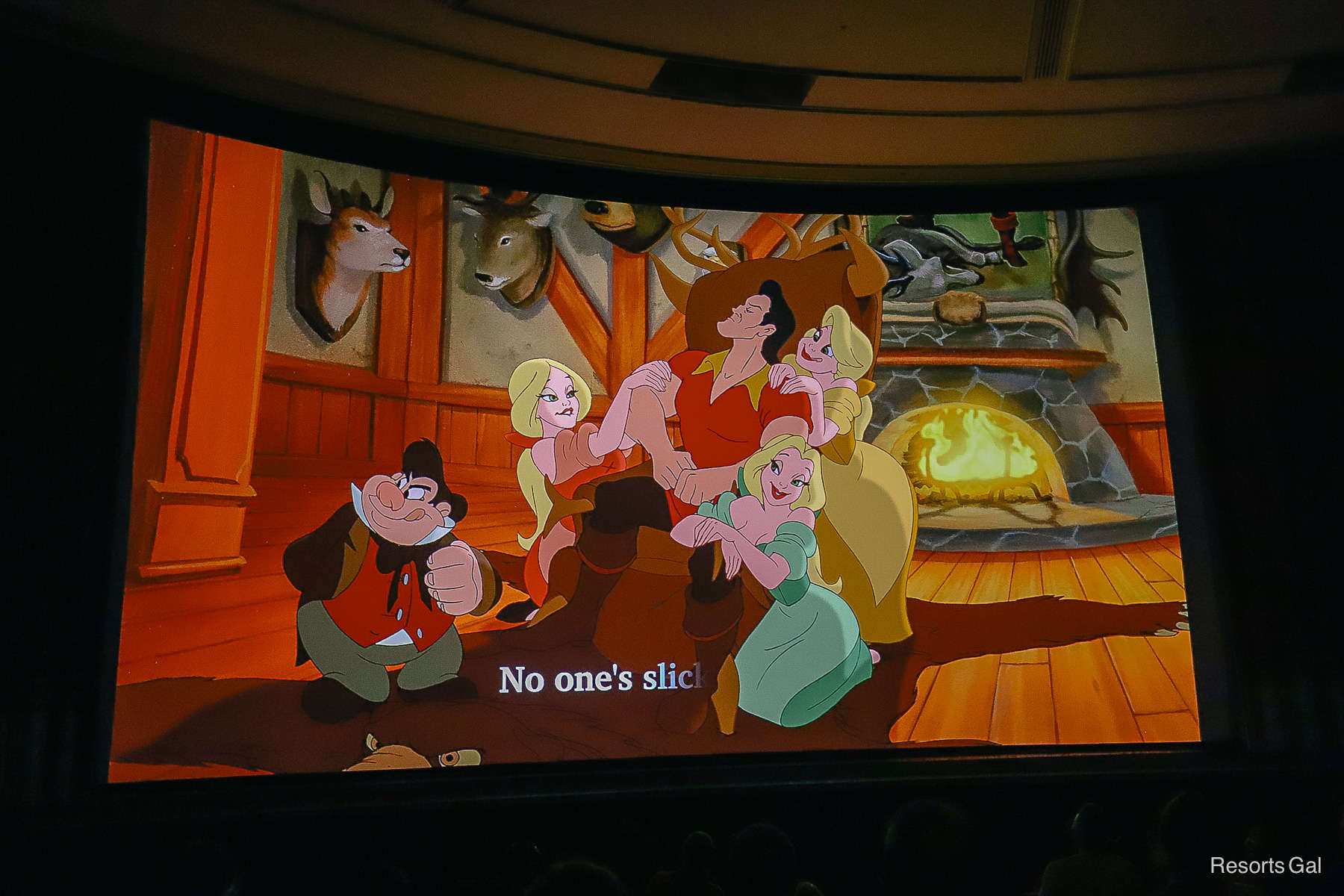 Gaston surrounded by women in front of a fireplace. 