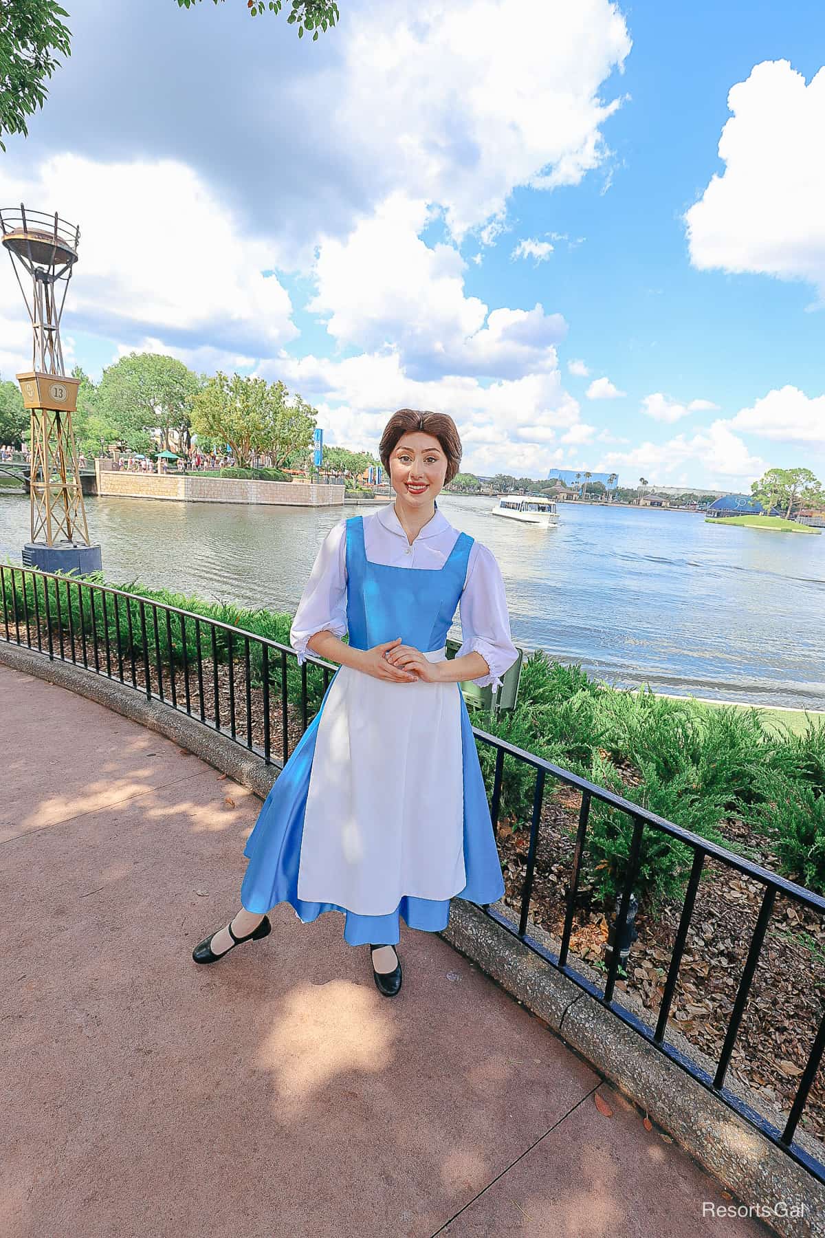 Belle poses for a photo with a boat in the World Showcase Lagoon behind her. 