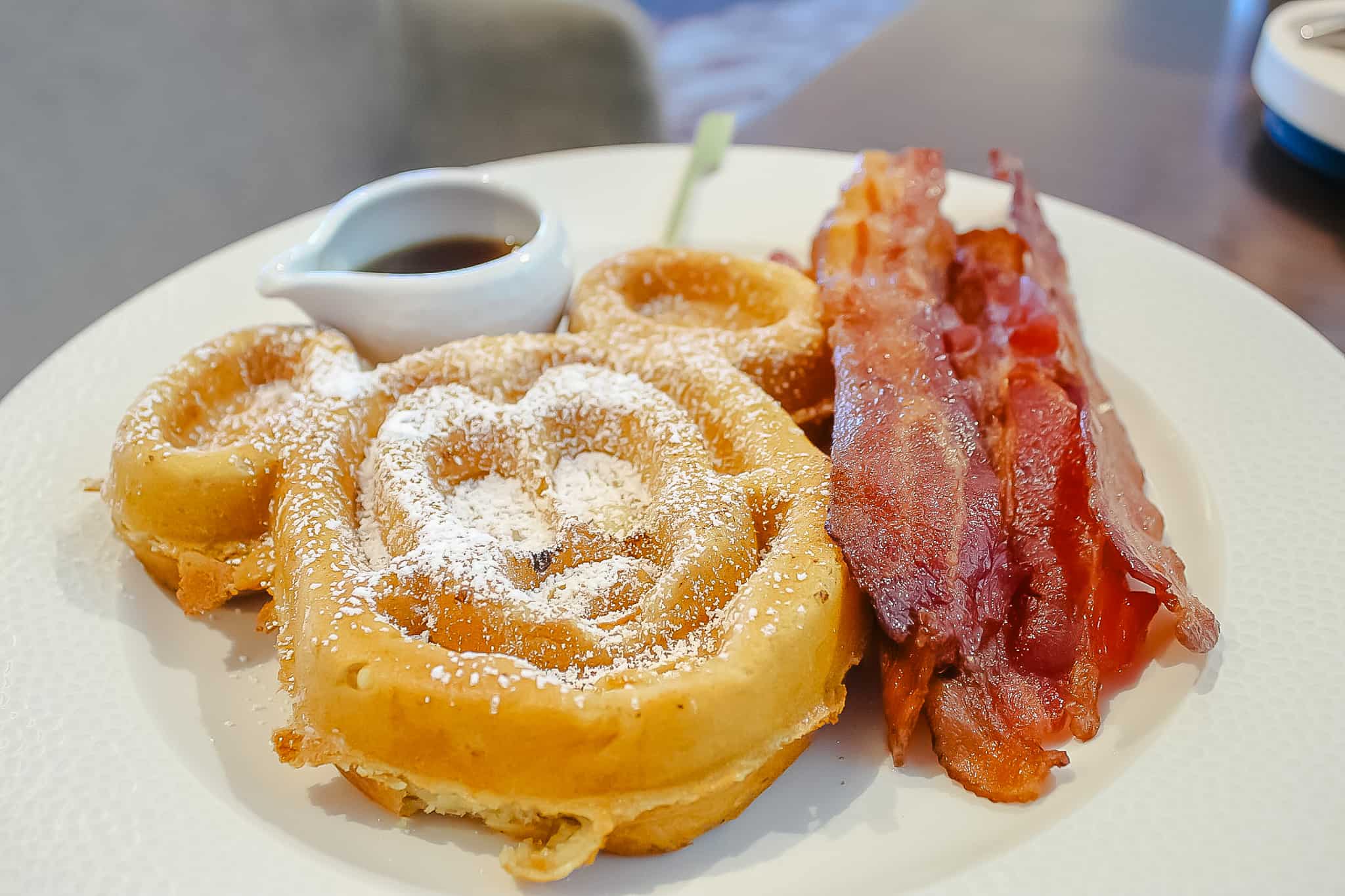 a Mickey waffle with syrup and a side of bacon 