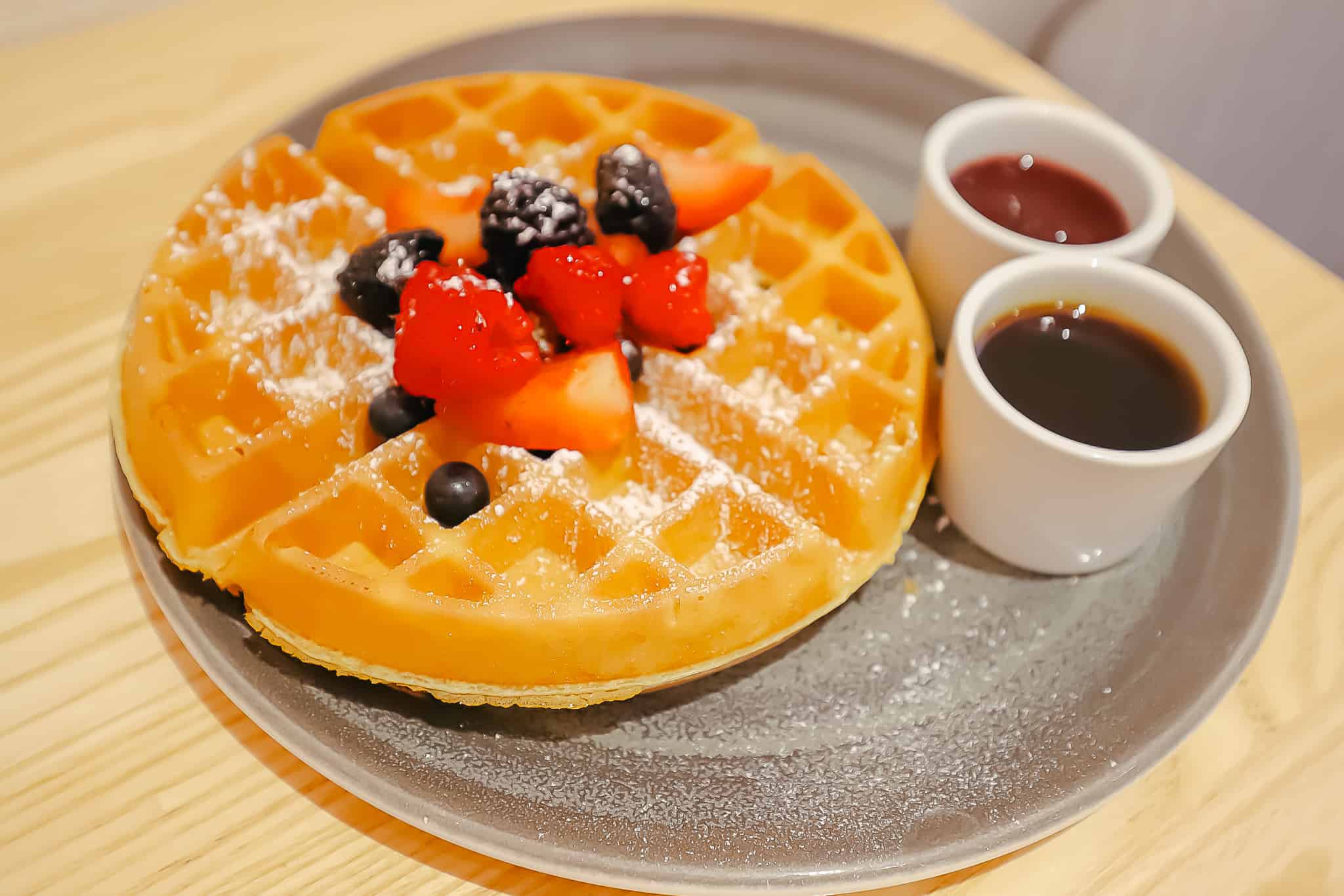 a plate with waffles, berries, and syrup 