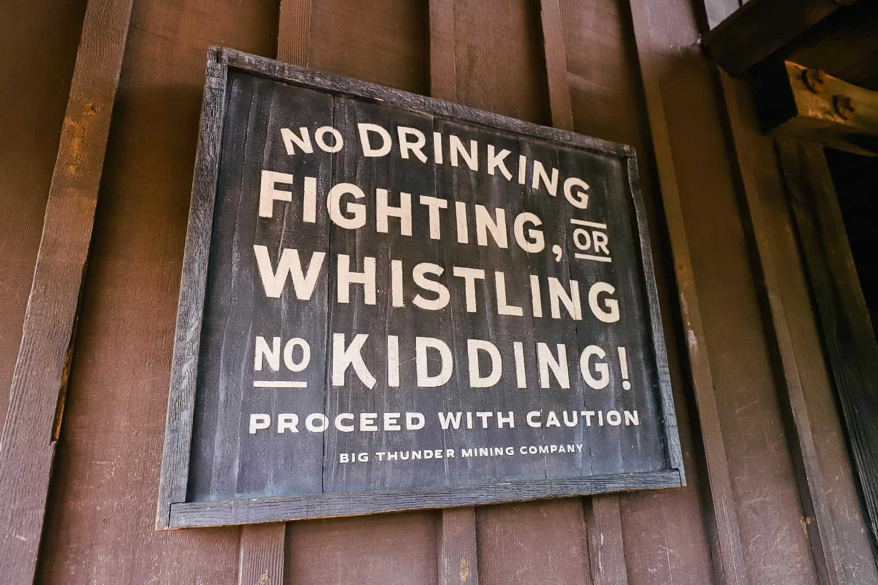 A sign that says No Drinking, fighting, or whistling, No Kidding, proceed with caution. 