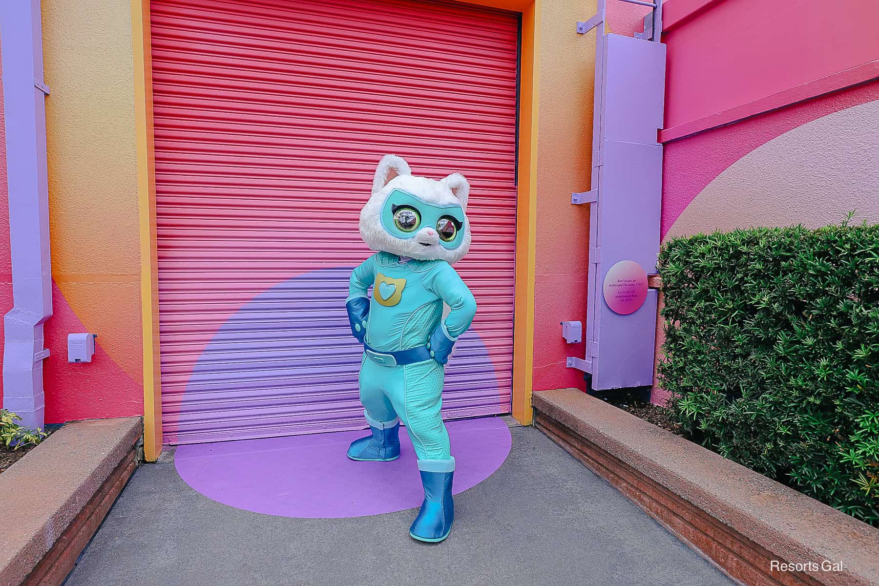 Bitsy poses with hands on hips in front of a vibrant backdrop 