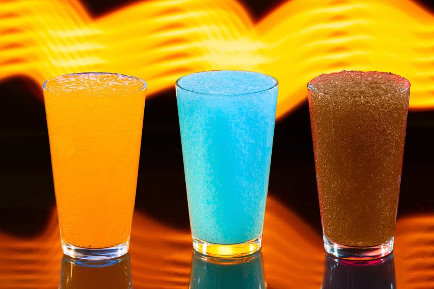 three frozen slushies in orange, blue and brown