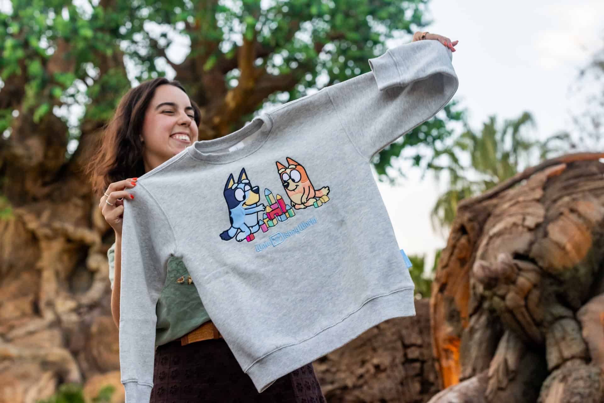 a person holding a grey Bluey and Bingo sweatshirt with the Walt Disney World logo 