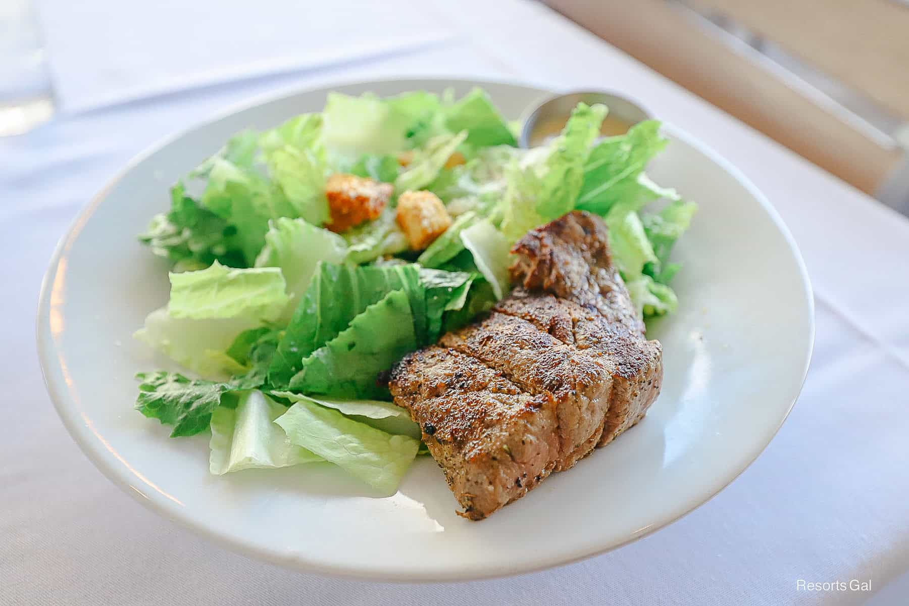 an angle of the Caesar Salad with the Steak on the side of the plate 
