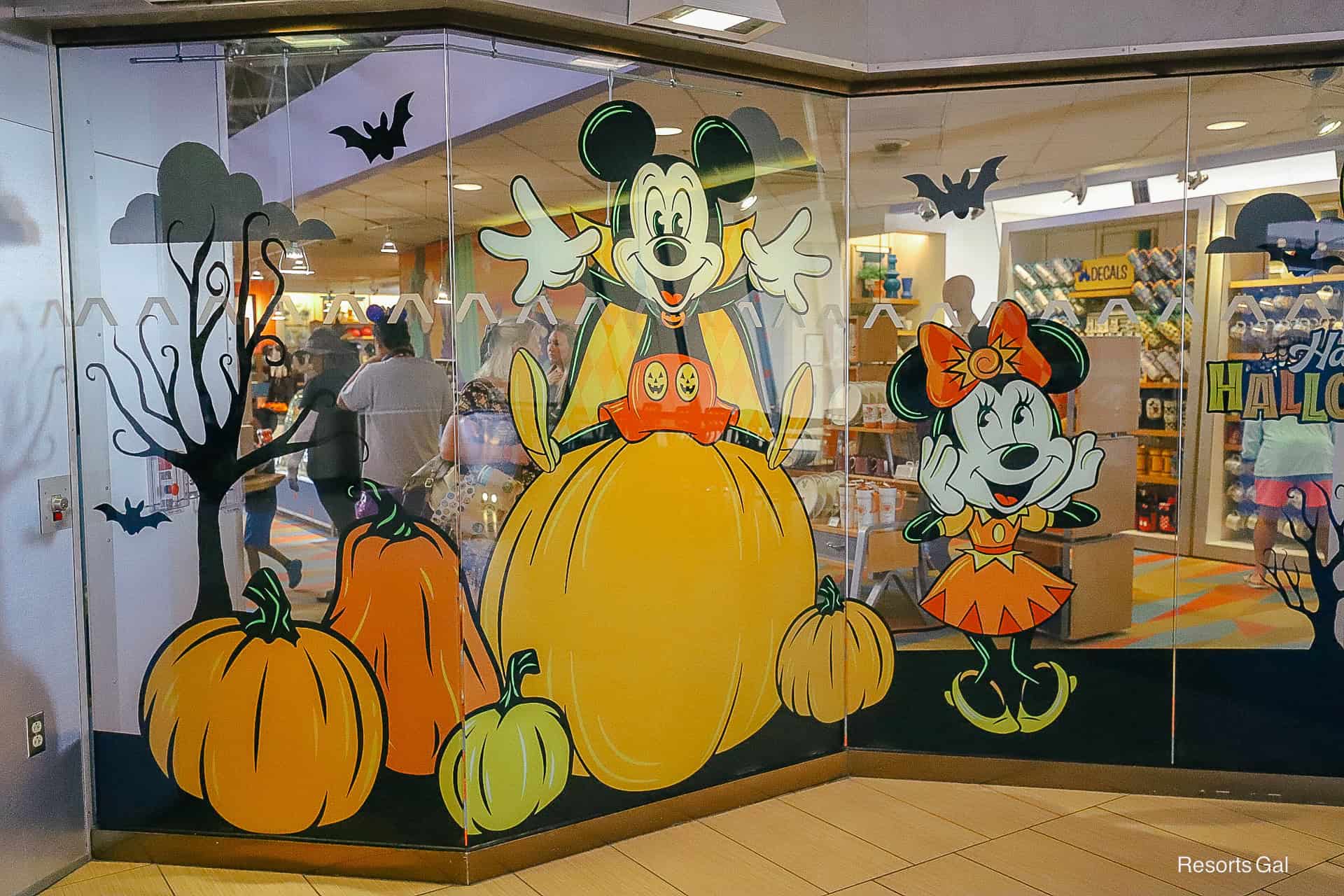 a closeup of Mickey sitting on pumpkins wearing a black and orange cape on the window display