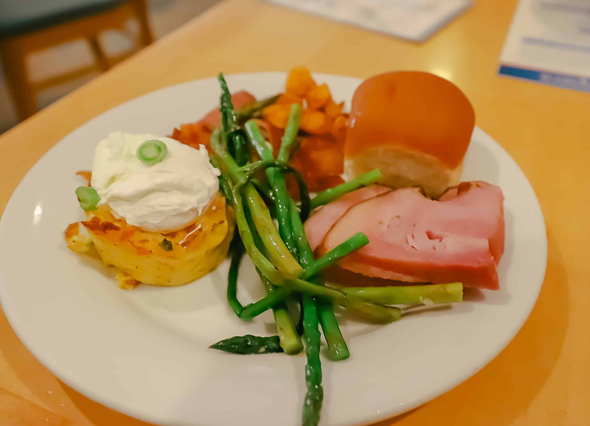 A prepared plate with a roll, ham, asparagus, poached eggs, and potatoes. 