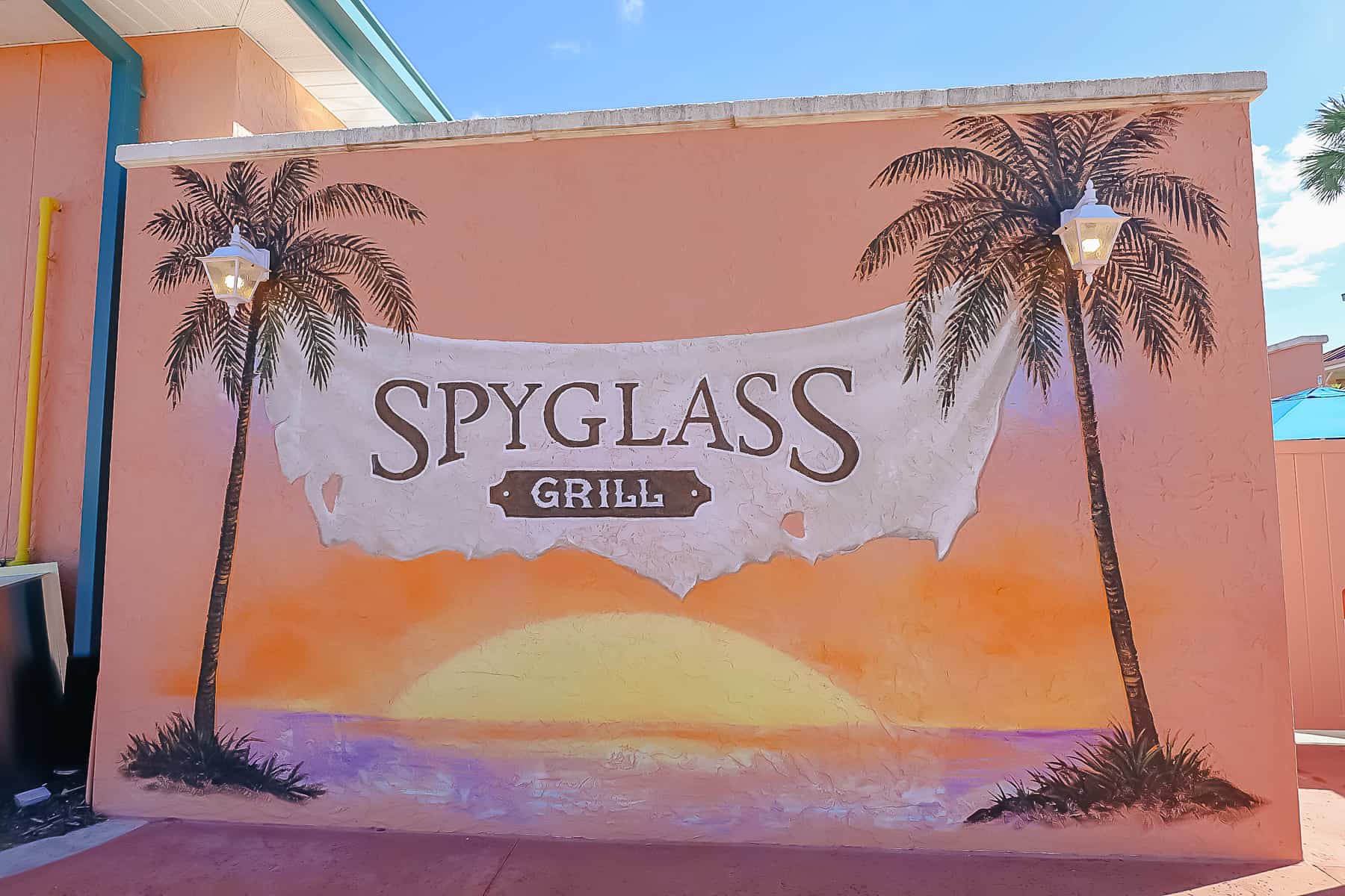 A mural that reads Spyglass Grill flanked by two palm trees and a sunset. 