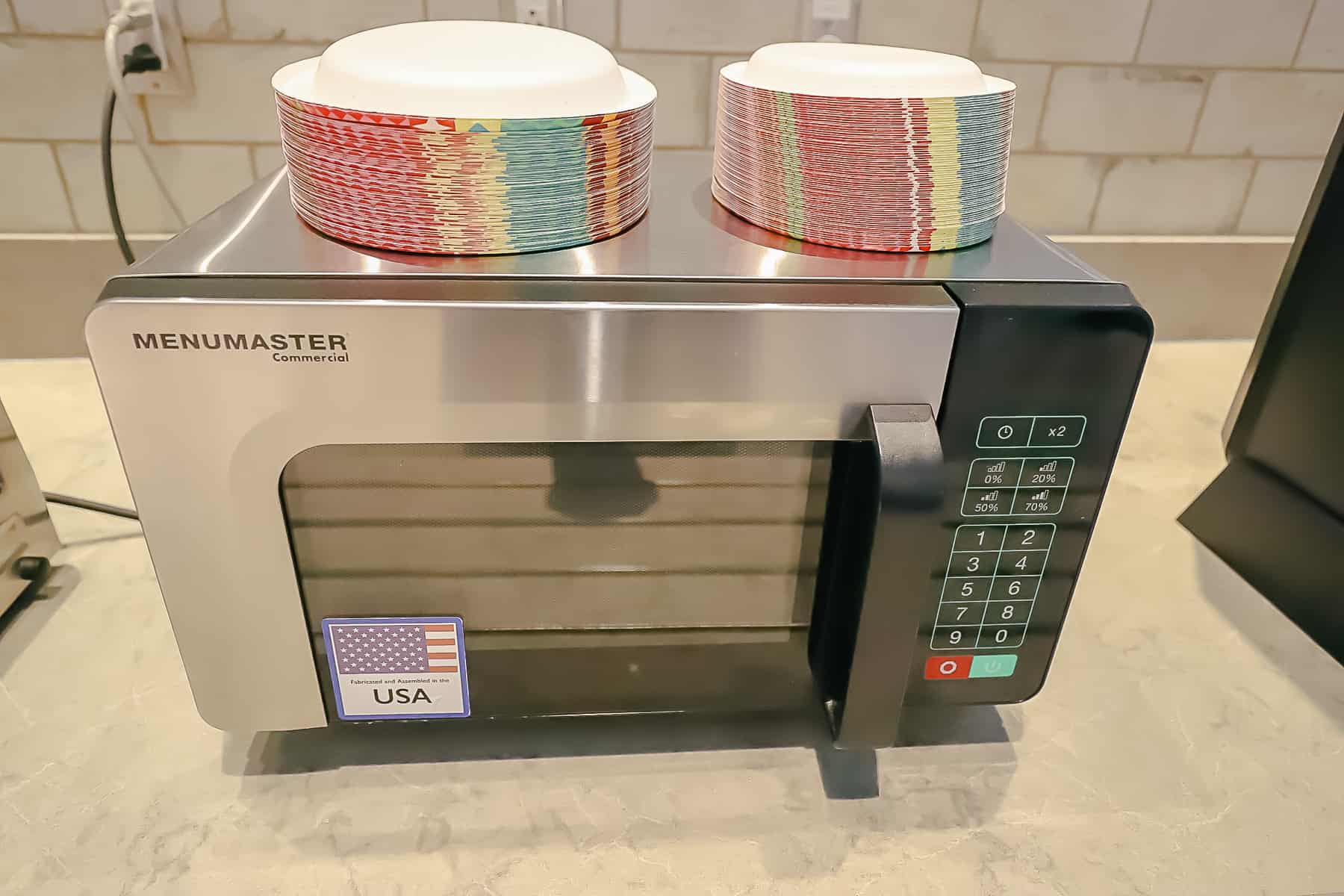 A microwave with paper plates stacked on top of it. 