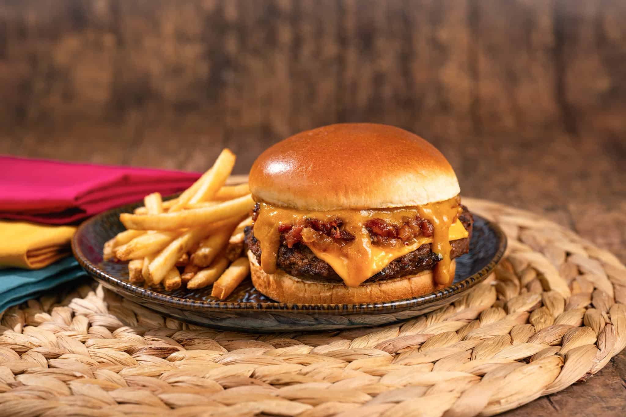 Cheeseburger with bacon and fries on a black plate