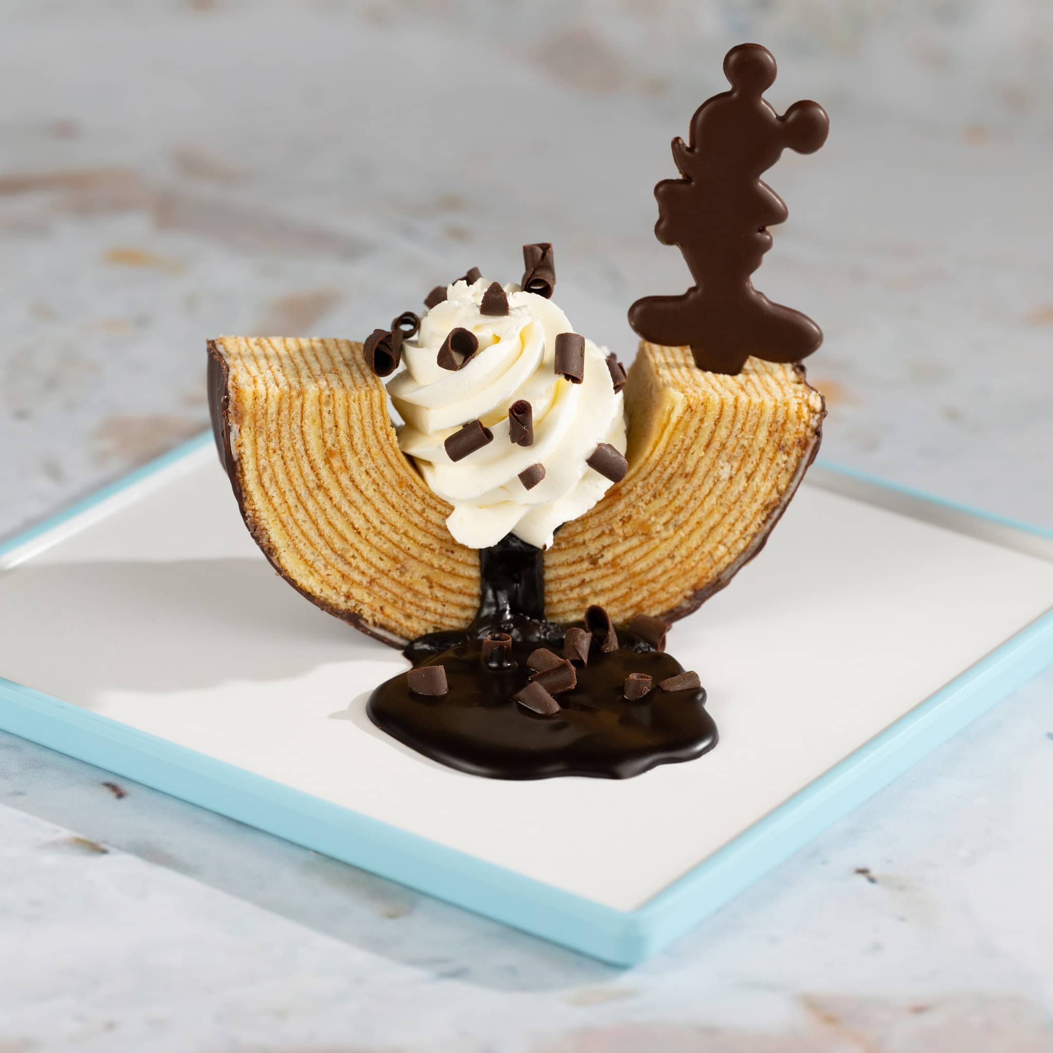 a baumkuchen dessert topped with whipped cream and a chocolate Mickey 