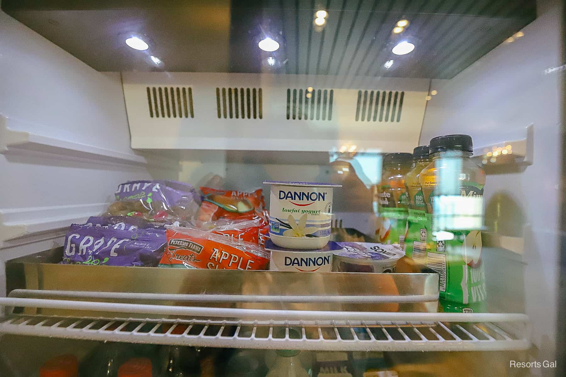 items in the fridge like bags of grapes, apple slices, yogurt and apple juice