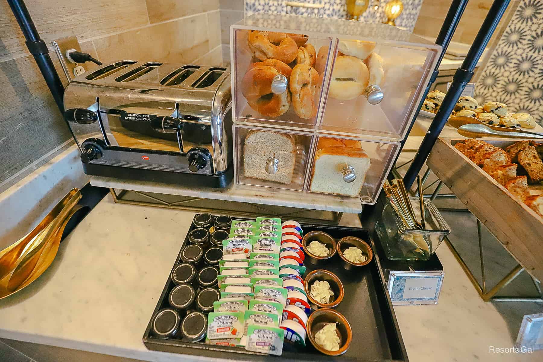 a bread box with drawers filled with bagels and toast, a toaster oven, various jellies and spreads 