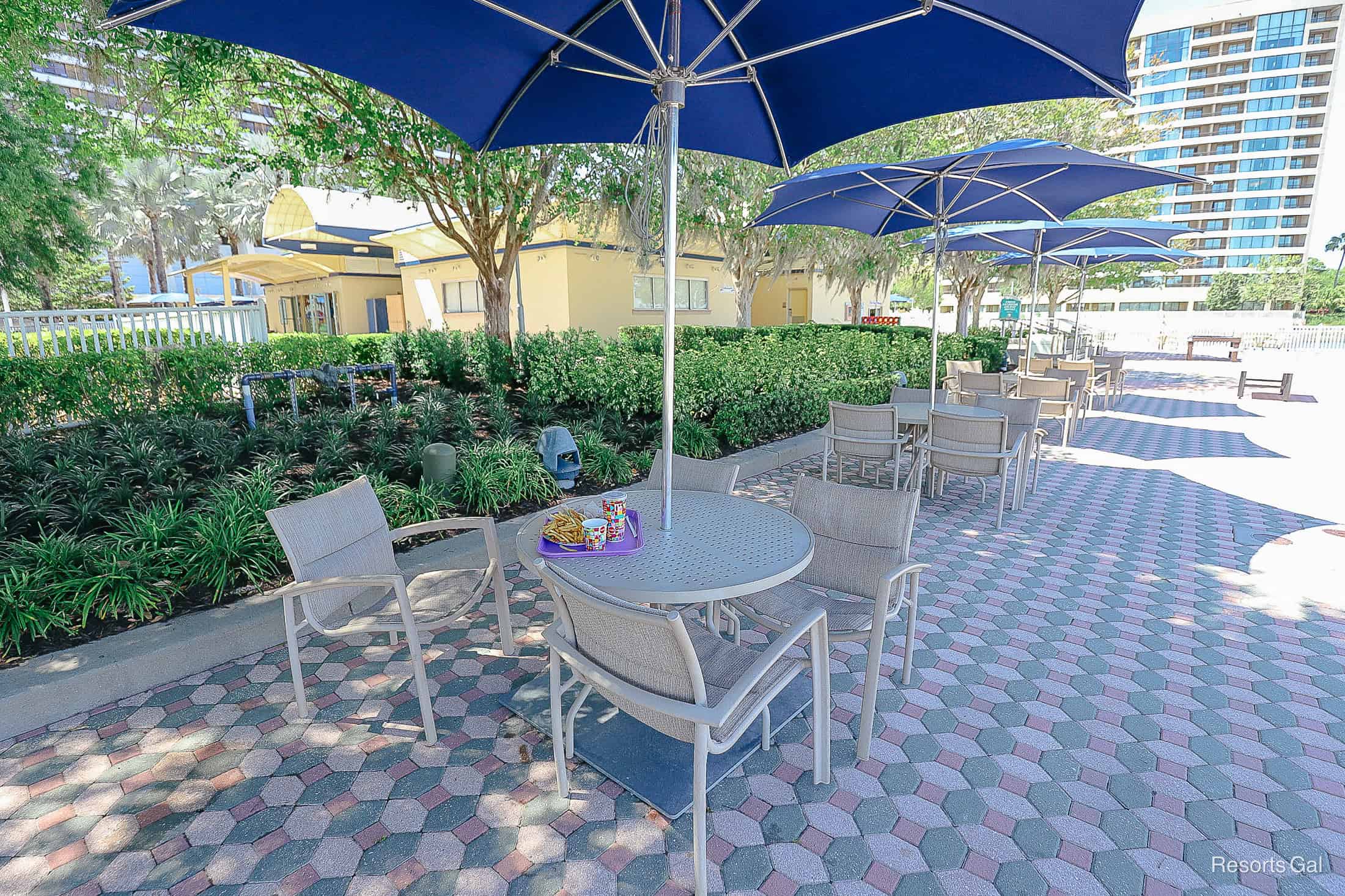 a row of tables and chairs in the shade between the Contemporary and Bay Lake Tower 