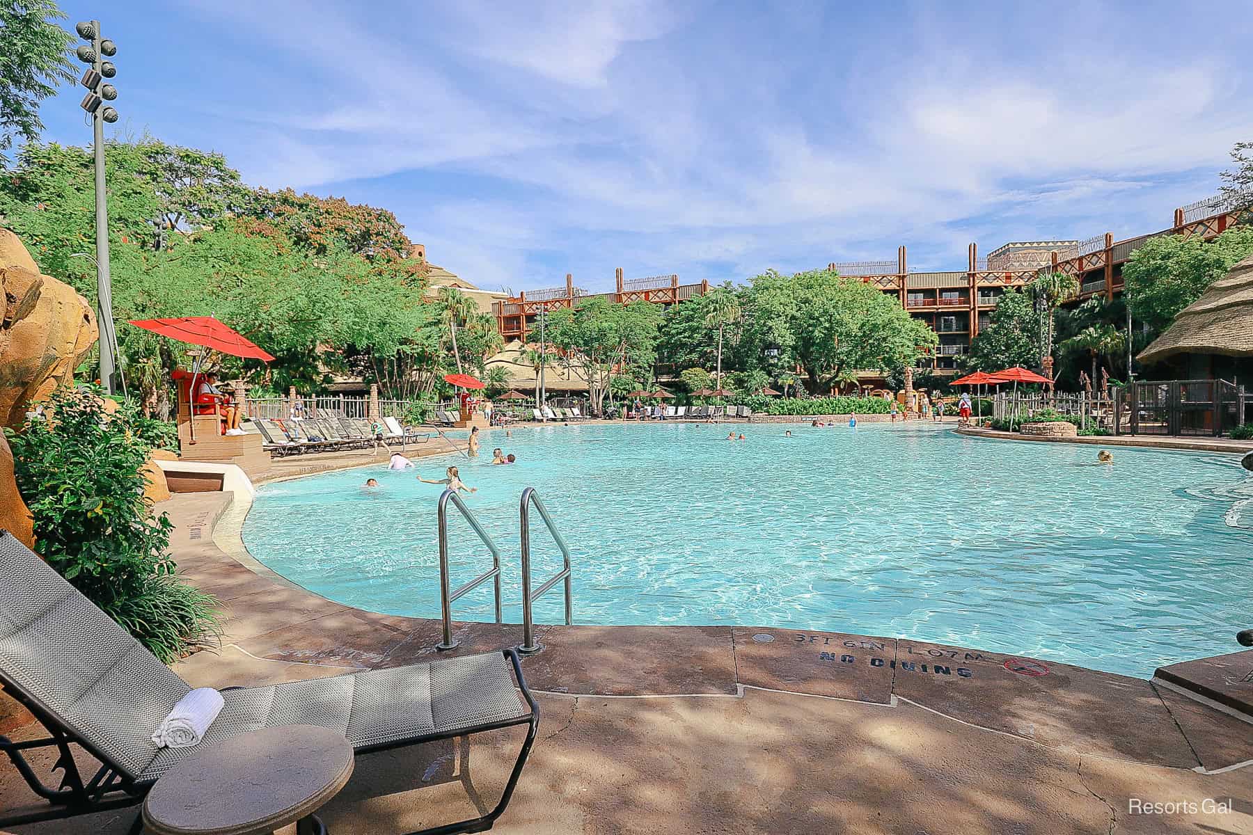 a lounger with a folded towel and side table by the pool 