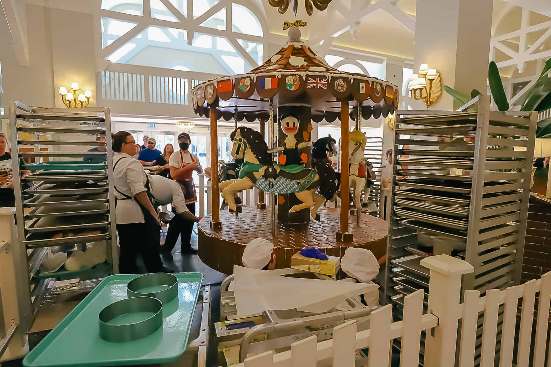 Chefs surrounded by sheet tray racks and other things used to create the gingerbread carousel. 