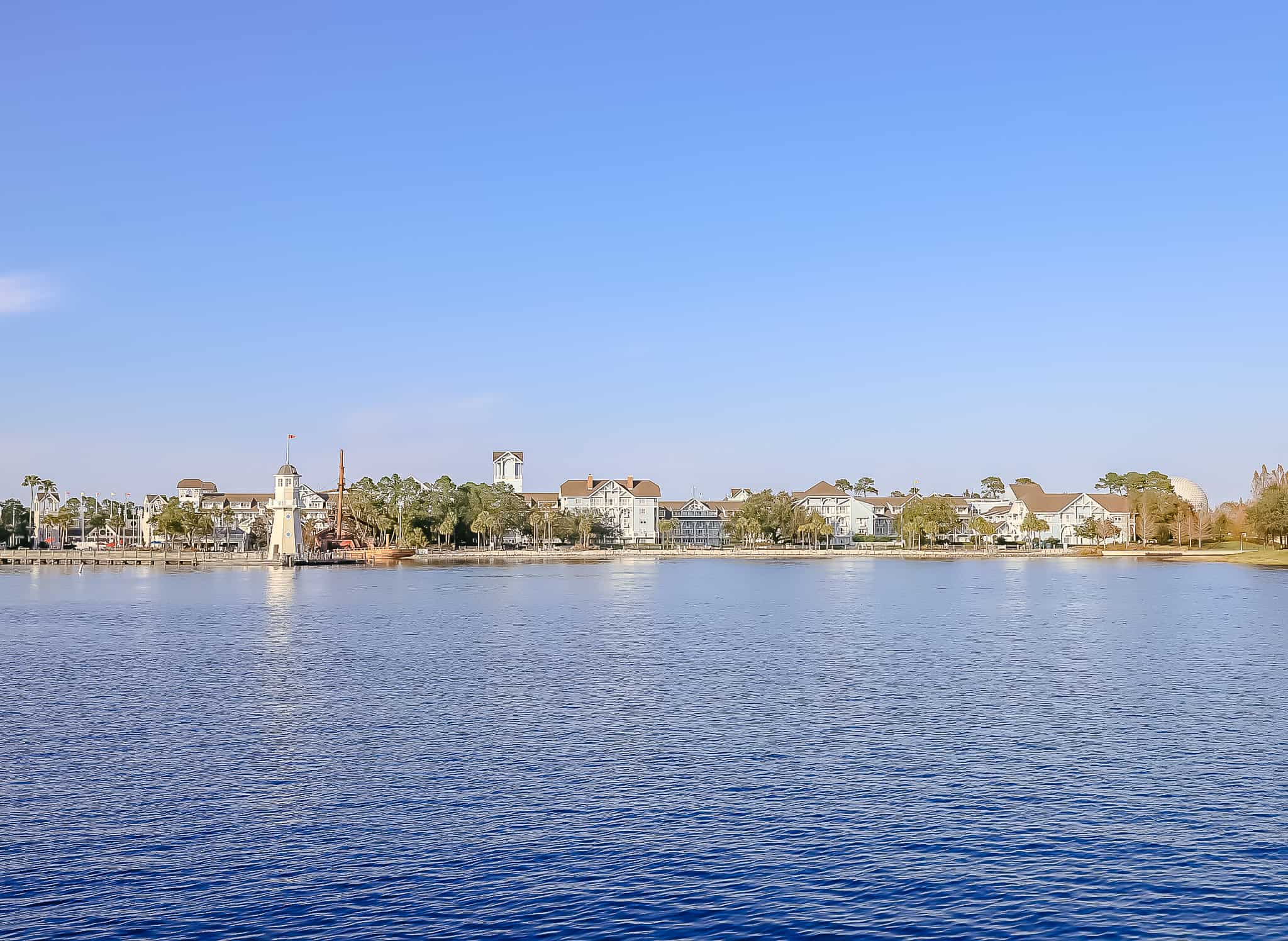 A wide angle of Disney's Beach Club sitting on the shore of Crescent Lake with Epcot's Spaceship Earth behind it.