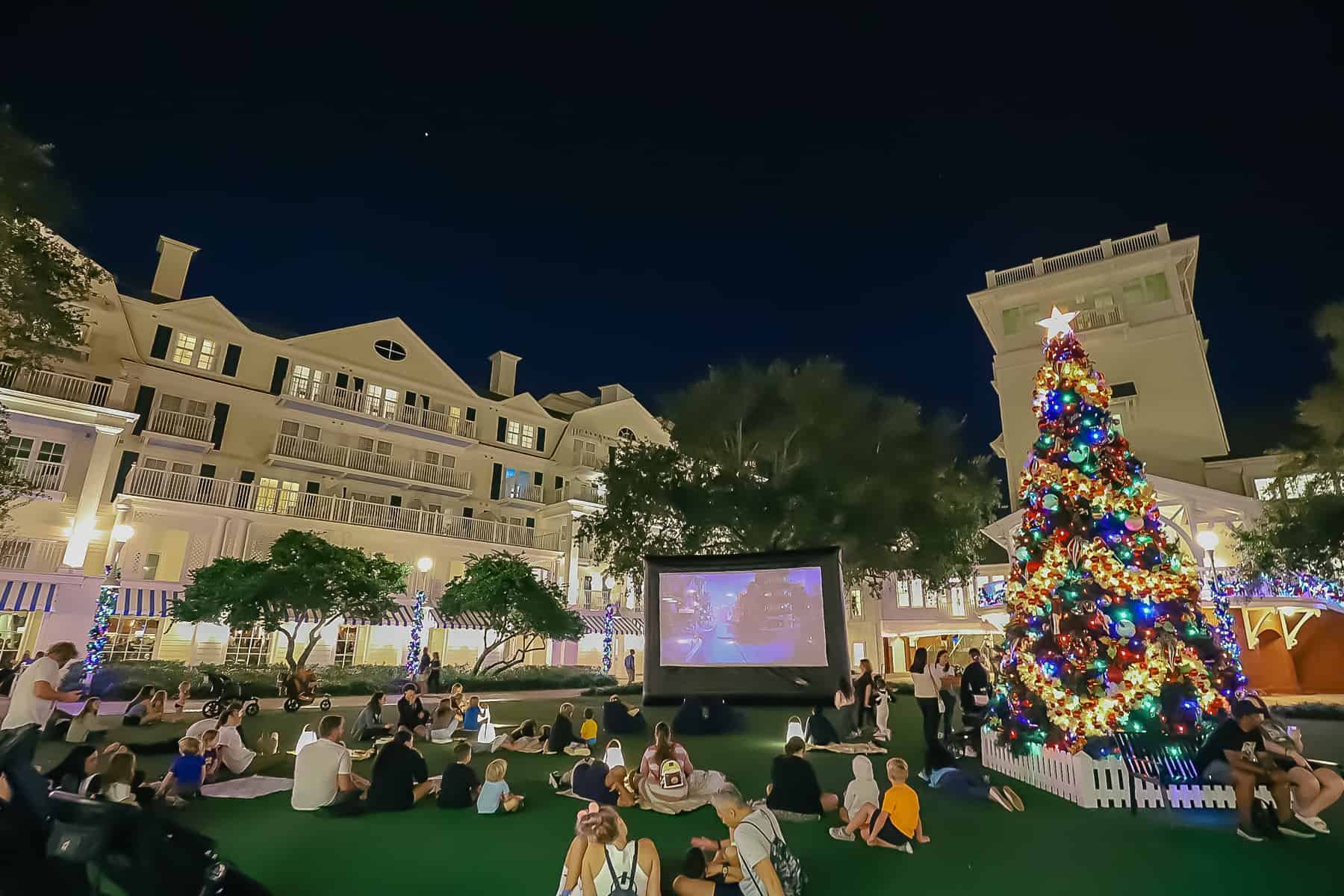 families enjoying a movie on the lawn next to the outdoor Christmas tree at Disney's Boardwalk