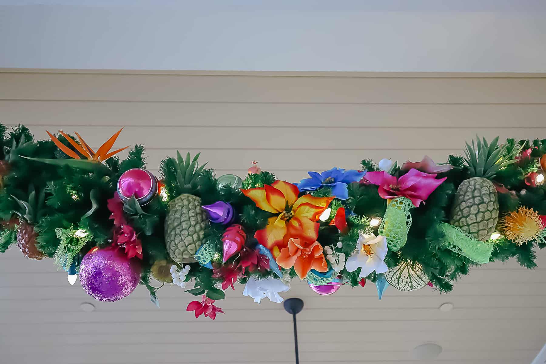 A close up that shows two pineapples and tropical flowers in the garland. 