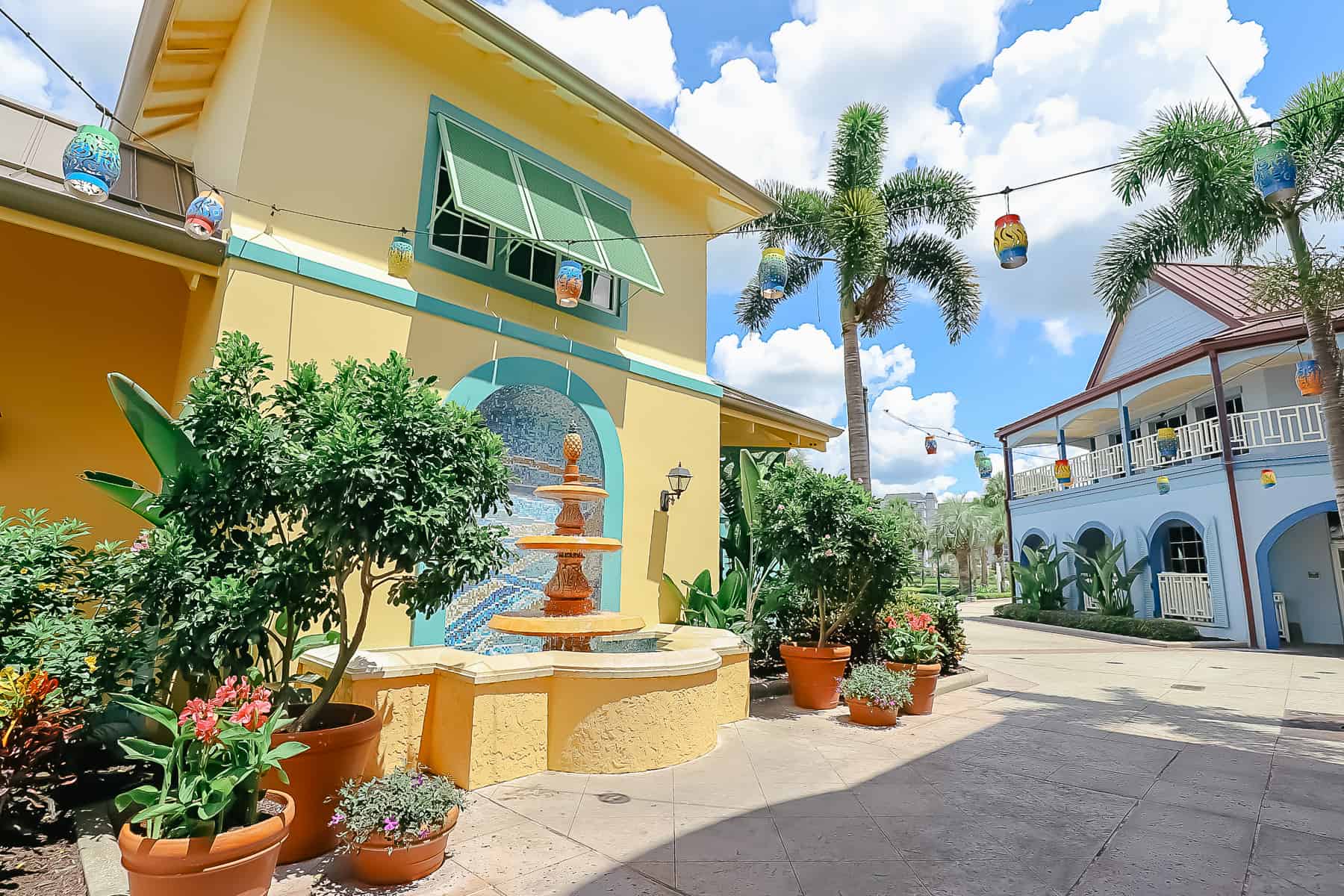 A decorative area that looks like the Caribbean with potted plants, a string of lights, and a fountain with a pineapple on the top and mosaic tile behind it. 