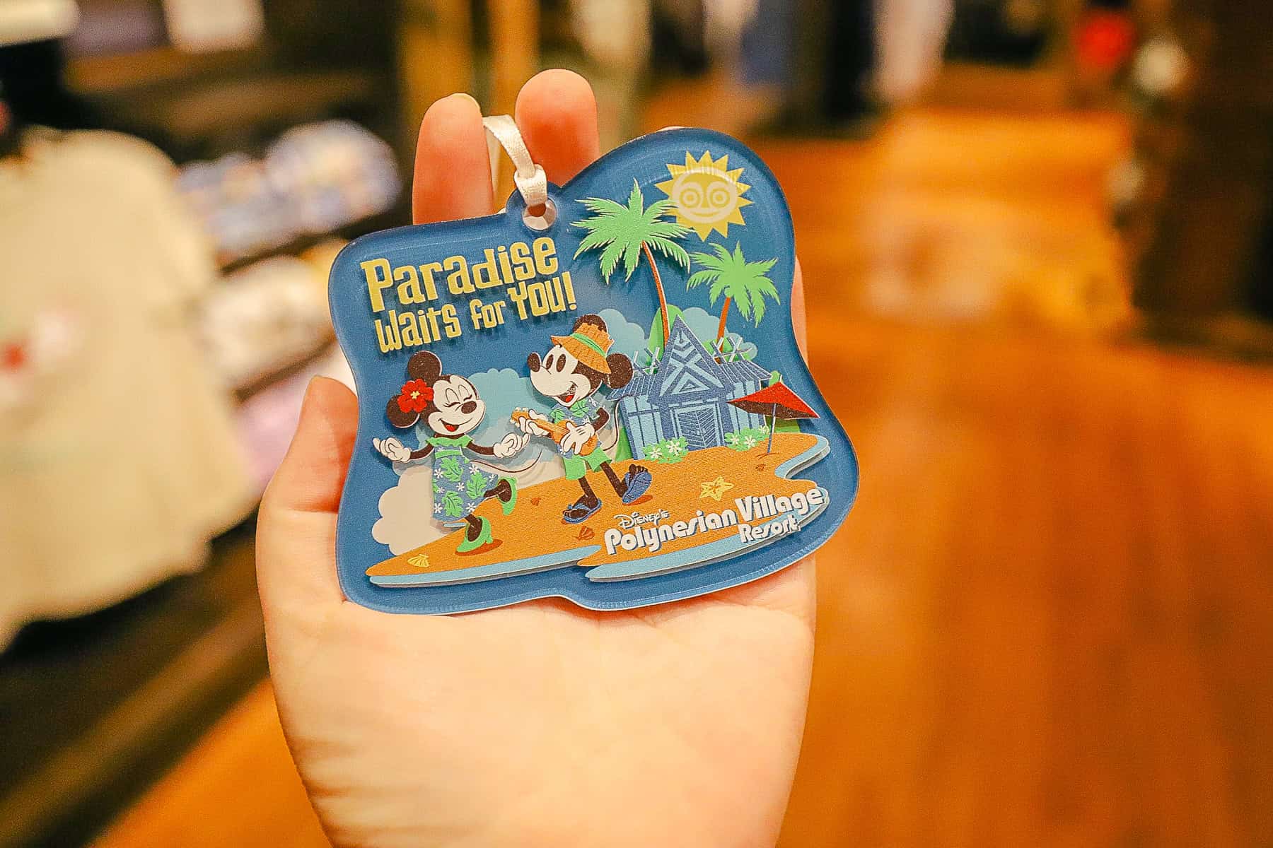 an ornament with the Polynesian's logo that says Paradise Waits for You