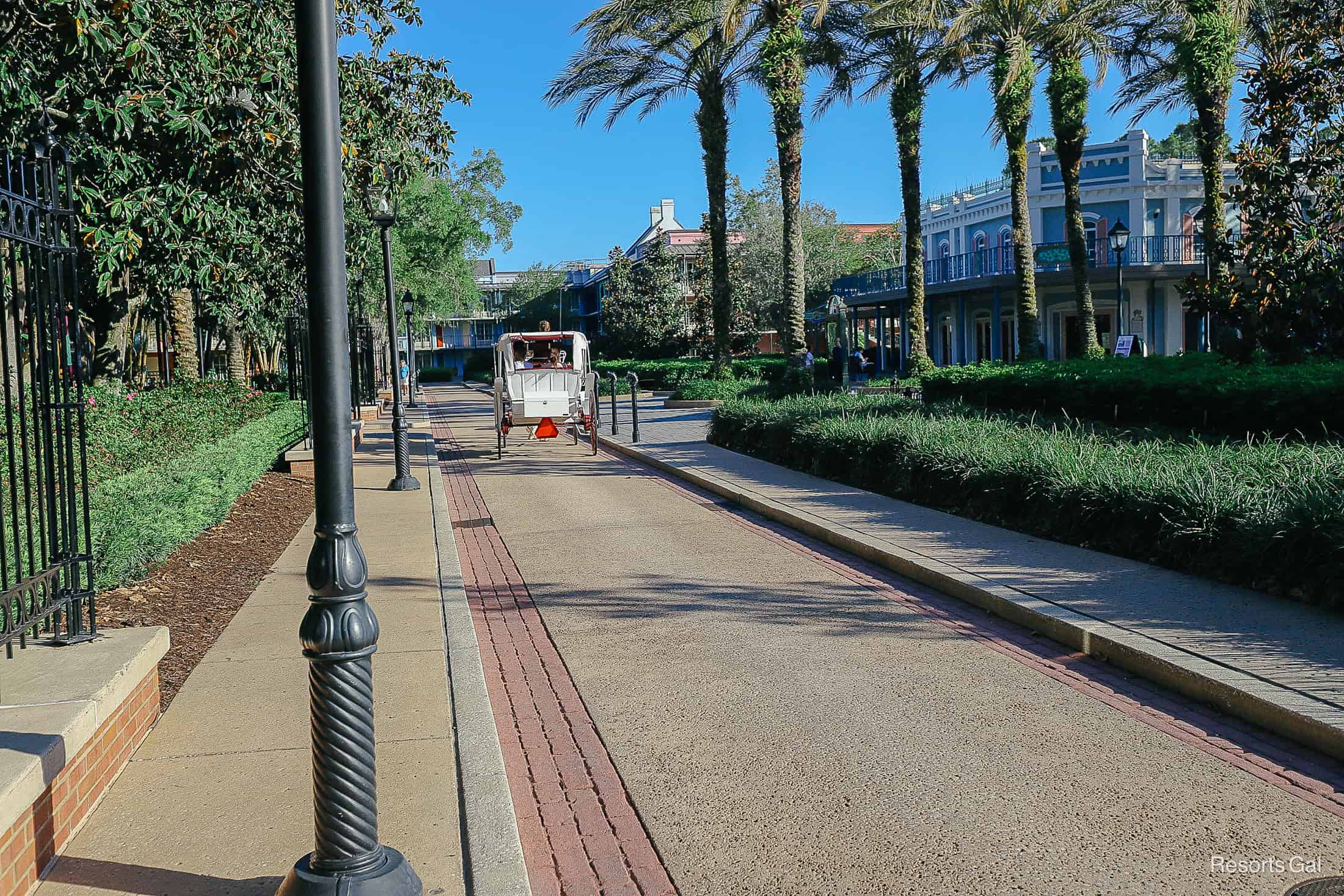 a sidewalk through French Quarter Resort with the back of a white horse drawn carriage in the distance 