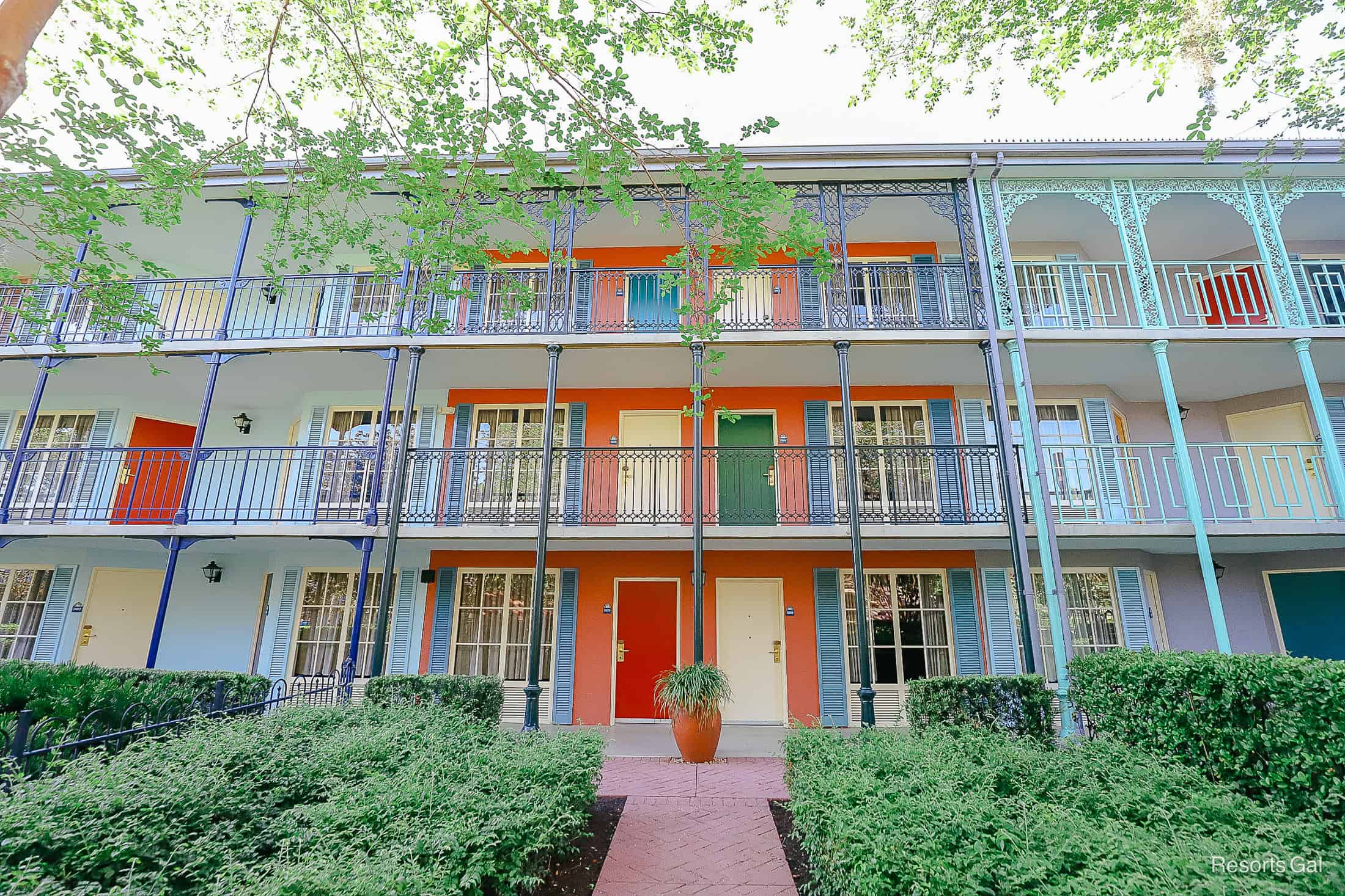 a front facing view of a building with coral paint and bright white, green, and red doors 