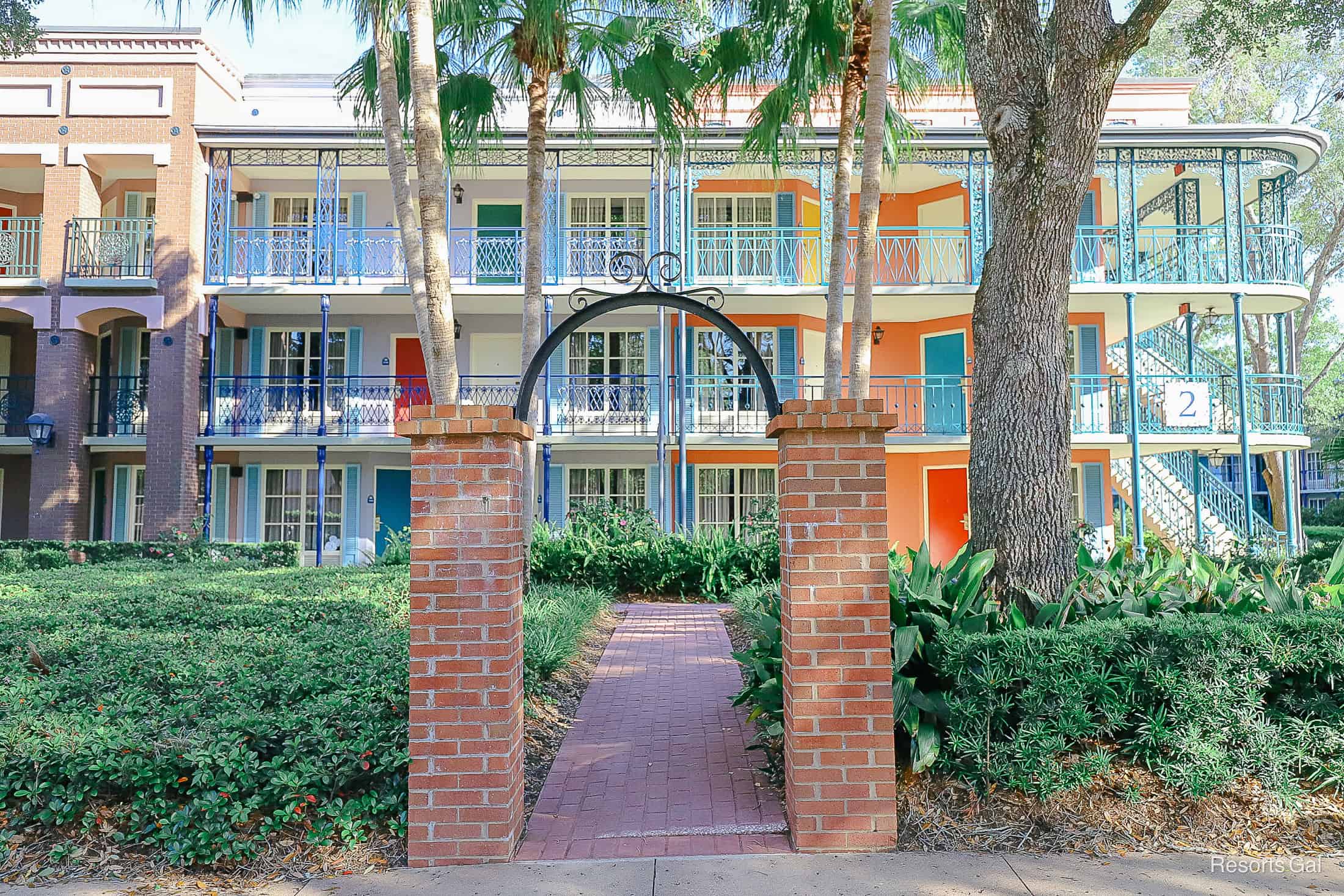 an arch with brick and iron in front of a building with brick pavers leading up to it 