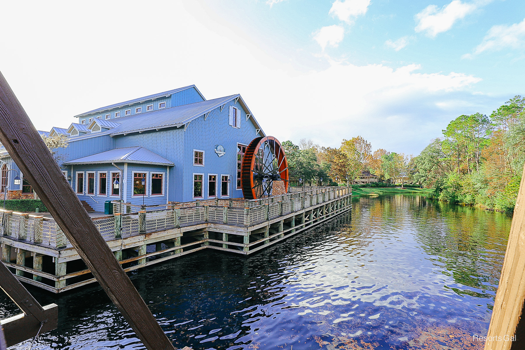 a blue building with a red water wheel sitting next to the river 