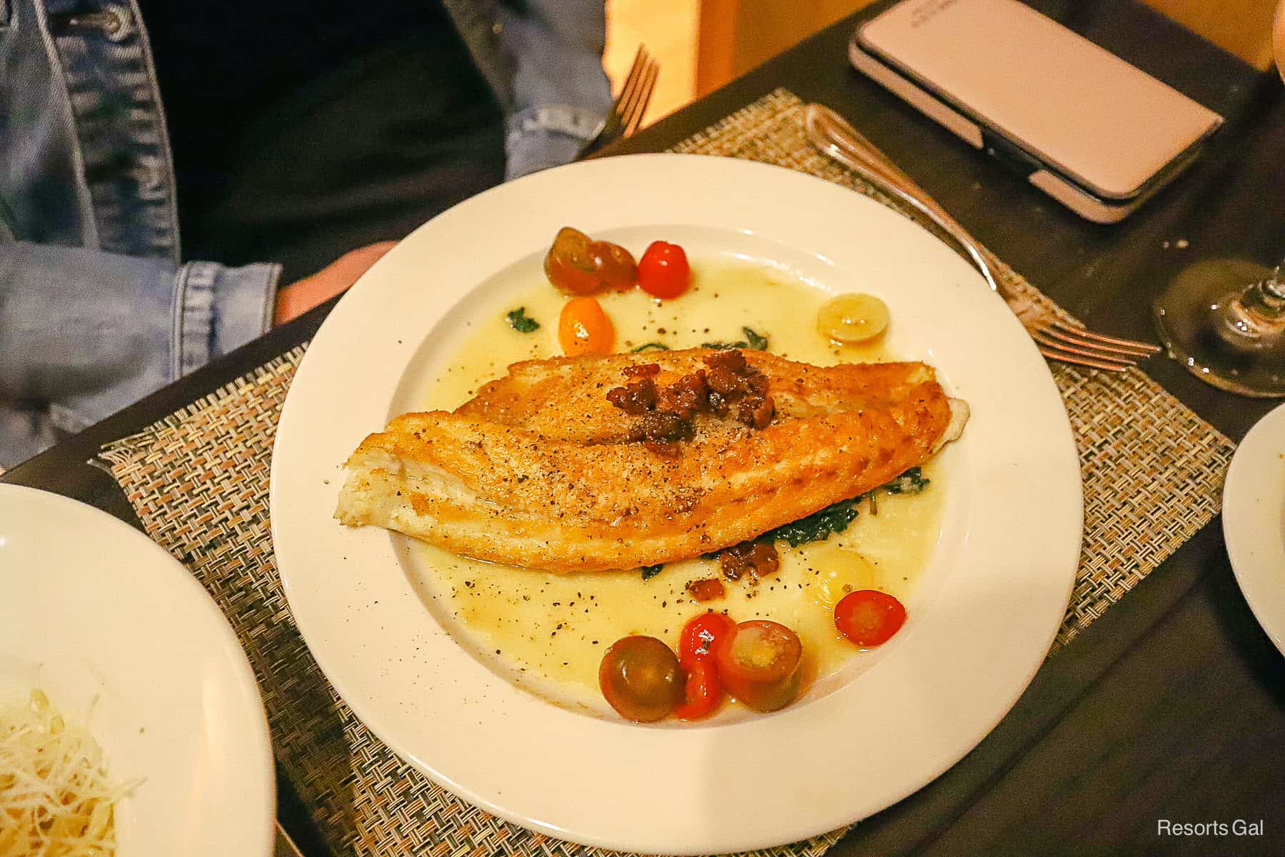 a plate with a filet of Branzino sitting on a bed of spinach with chopped cherry tomatoes