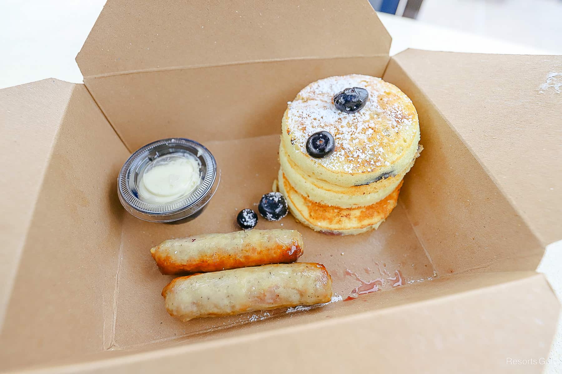 an order of lemon pancakes topped with blueberry and two sausages 