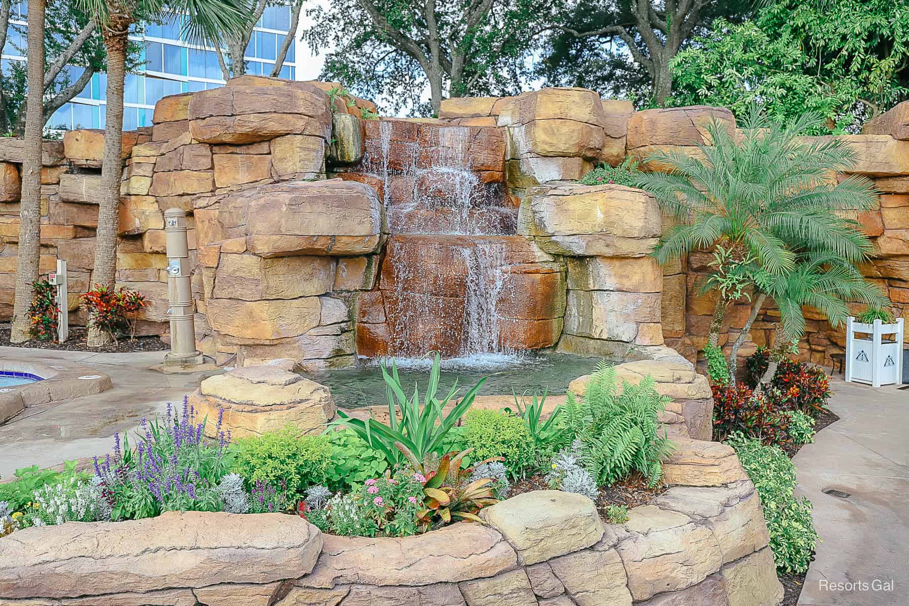 another waterfall that runs into a pool with pretty flowers and palm trees 