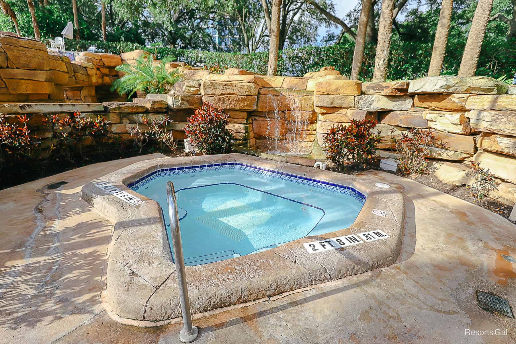 a hot tub nestled in a cover area by the pool with a small waterfall behind it 