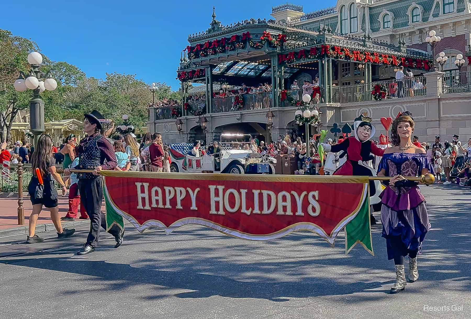 two villainous grand marshals lead the parade carrying a Happy Holidays banner